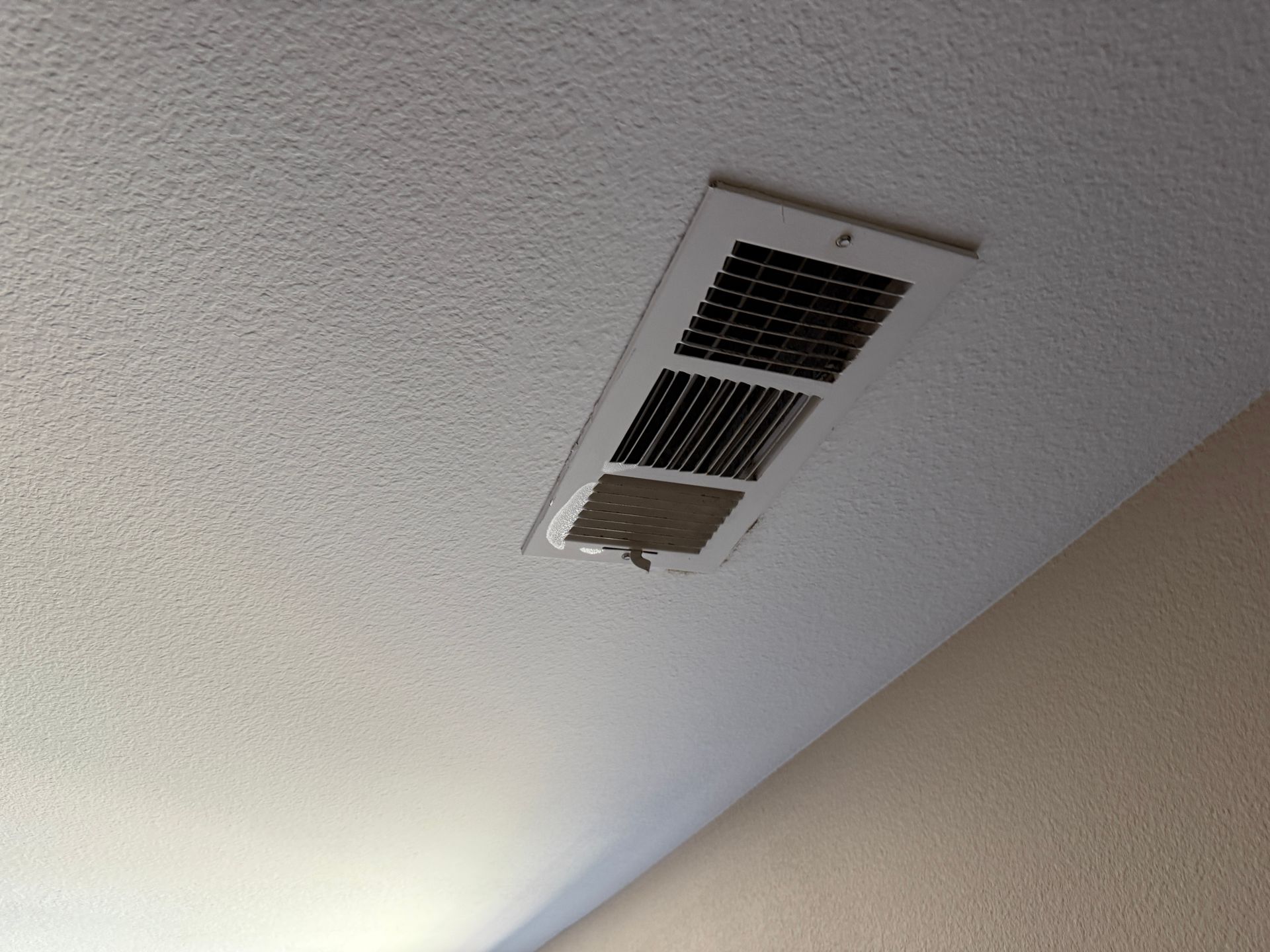 Ceiling air vent with open grille, viewed from below on a white textured ceiling.