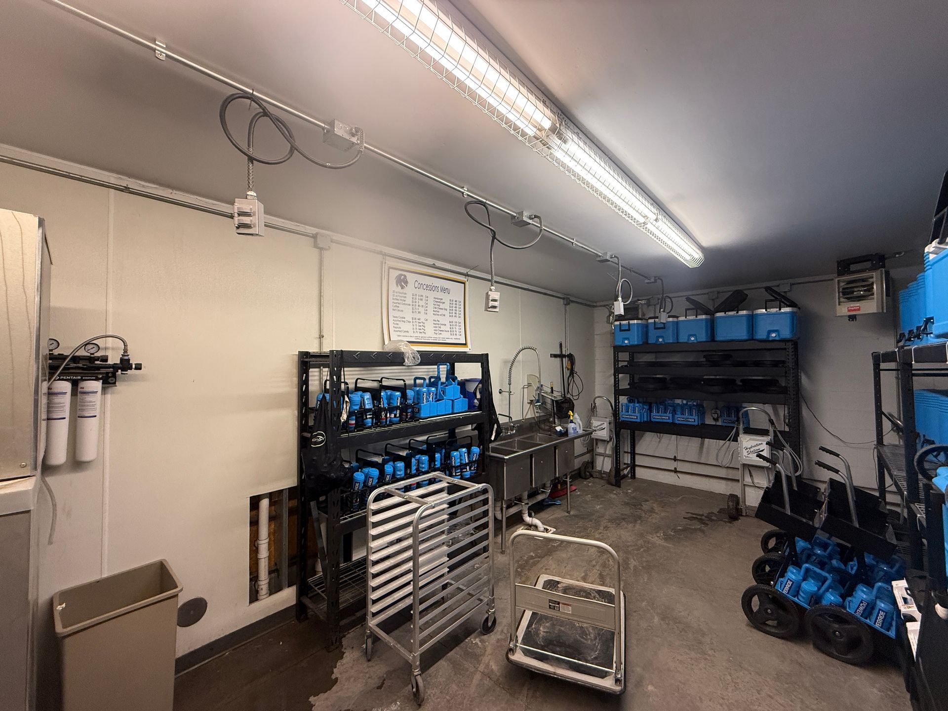 Workshop with shelves of blue tool bins, metal carts, and equipment under fluorescent lights