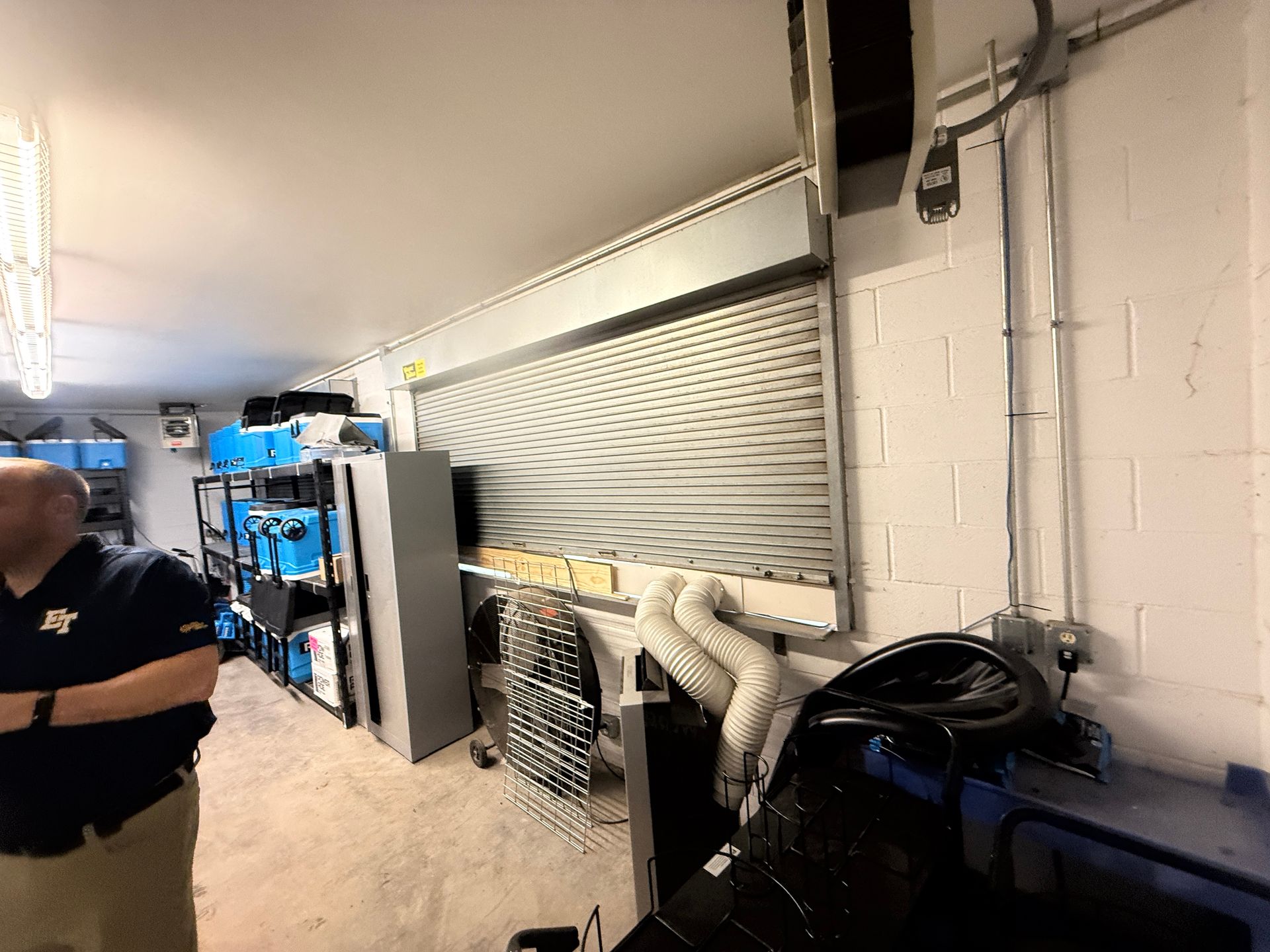Indoor utility room with a person standing near blue machinery, pipes, and a large vented wall panel