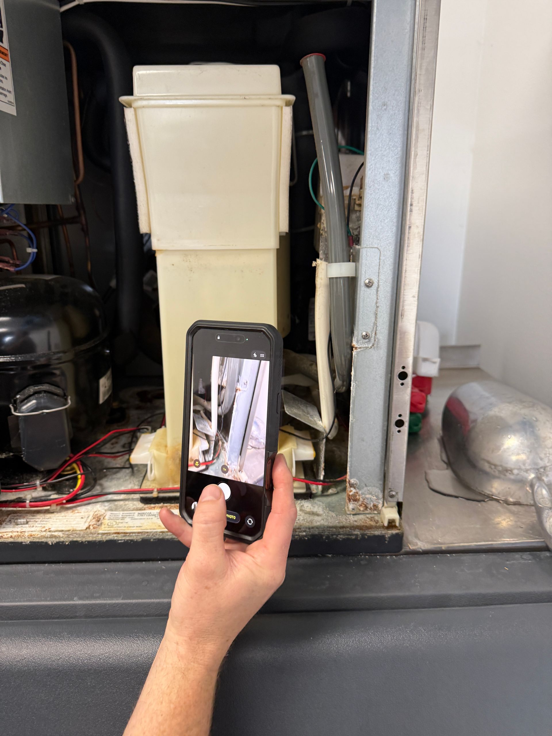Hand holding phone to photograph HVAC unit with open cabinet and exposed components