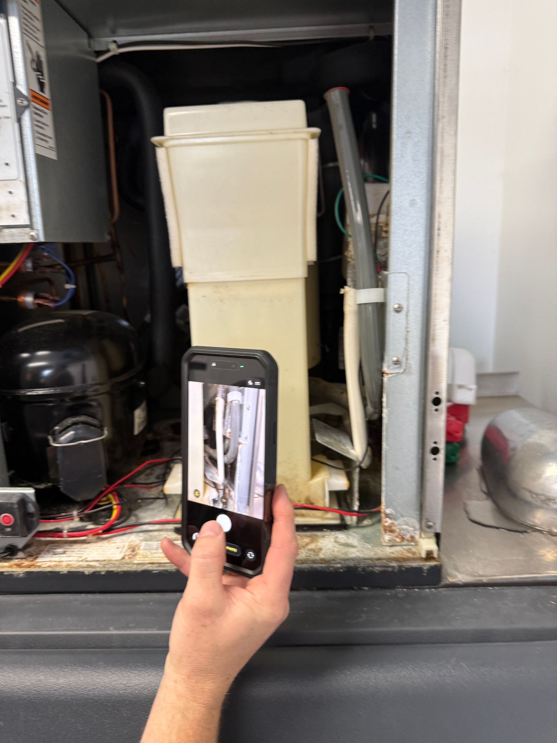 Hand holding a phone up to an open utility compartment with pipes, tank, and equipment inside