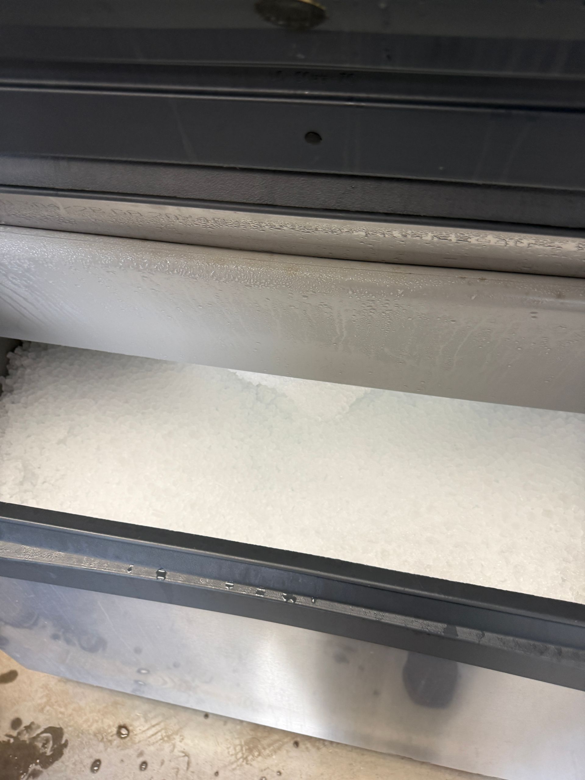 Snow piled against a metal threshold and glass door track, with wet floor below.