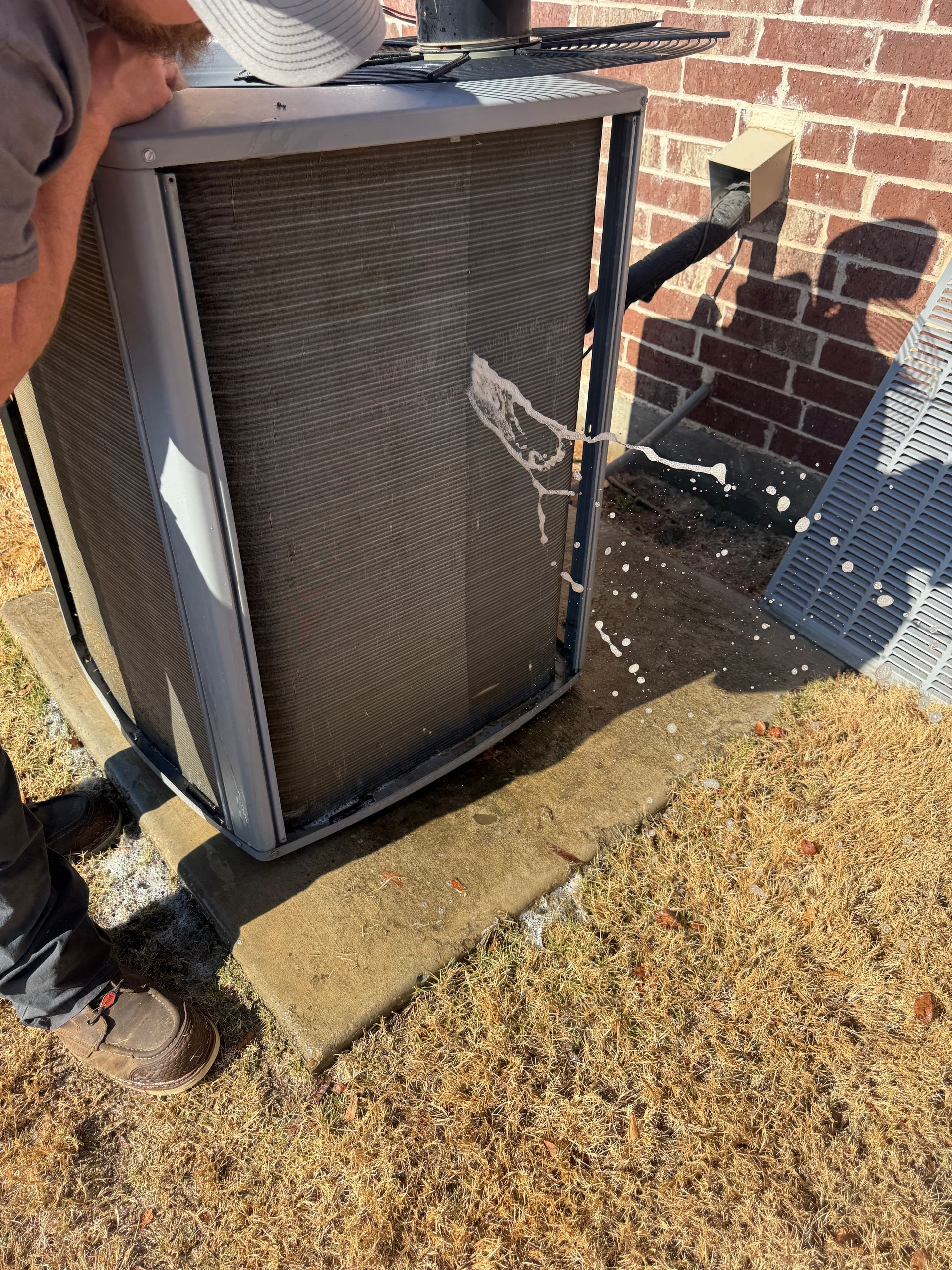 Person carrying a large outdoor air conditioner unit beside a brick house and lawn outside.