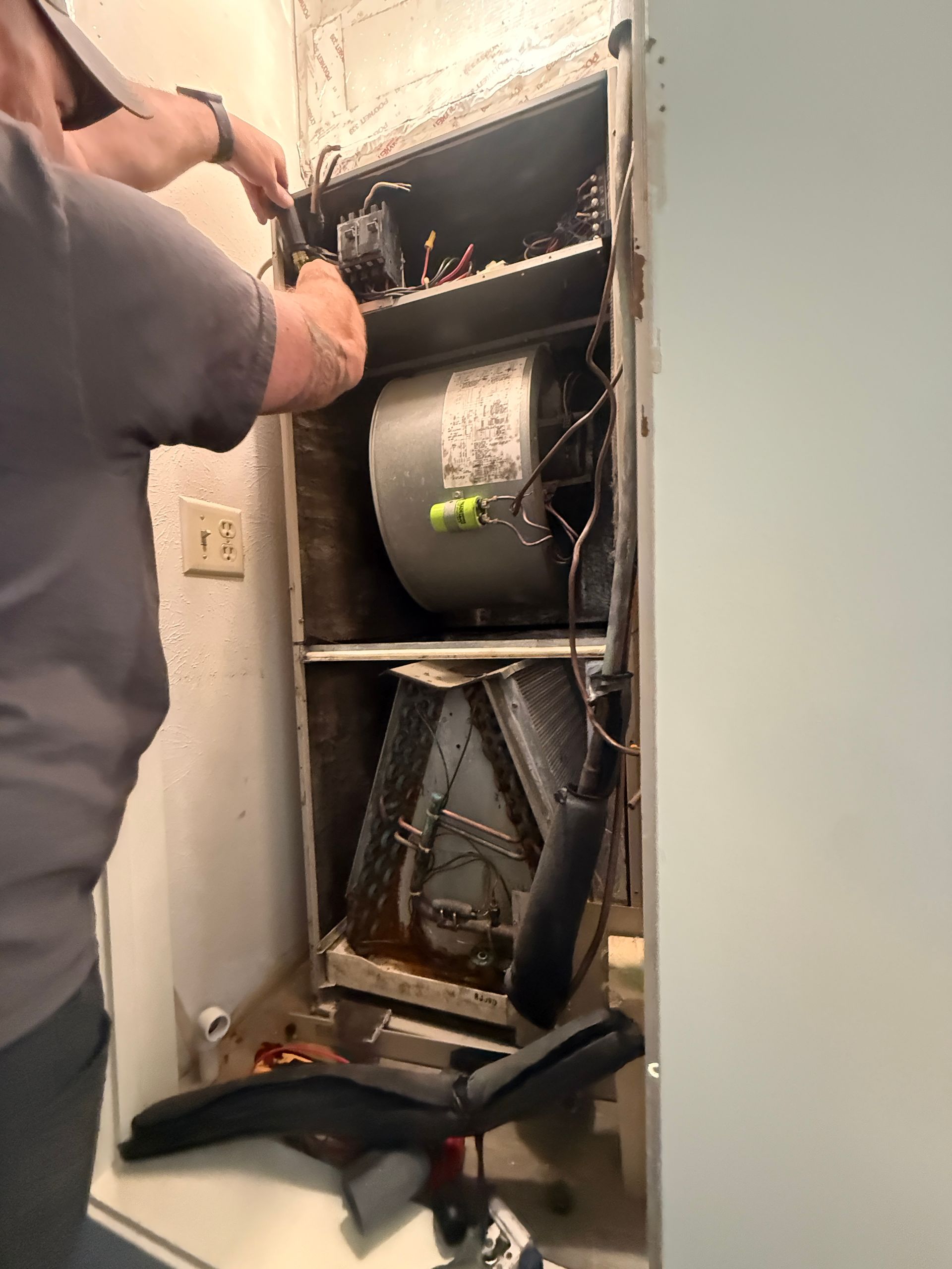 Technician repairing HVAC unit in a wall closet with exposed ductwork and tools.