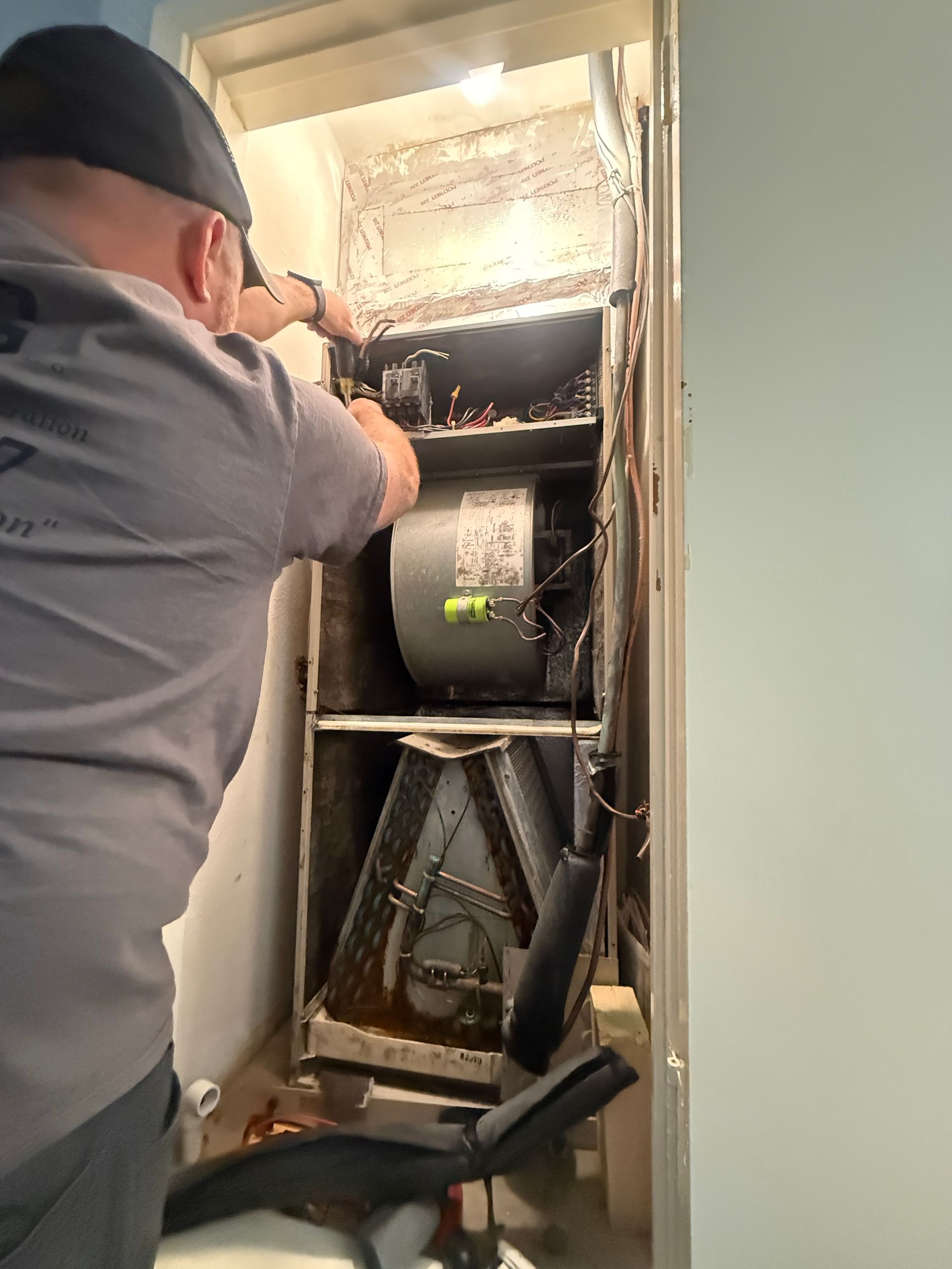 Technician working inside an open HVAC unit in a wall cavity