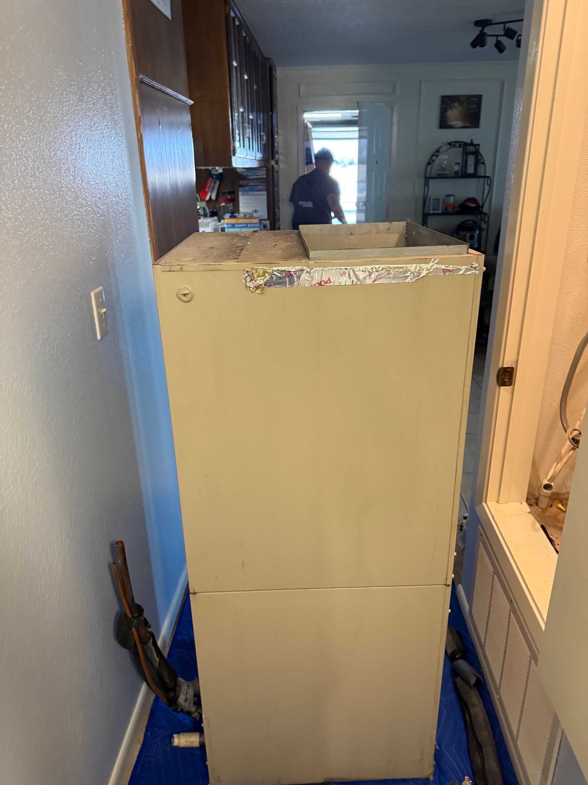 Narrow hallway with a tall white appliance blocking the way, with a person visible in the background.