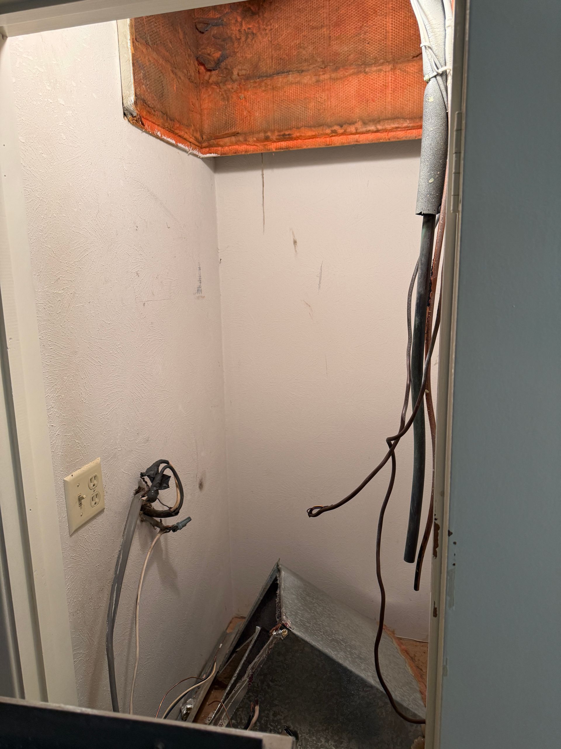 Narrow utility closet with exposed wiring, wall outlet, and an open ceiling vent or ductwork.