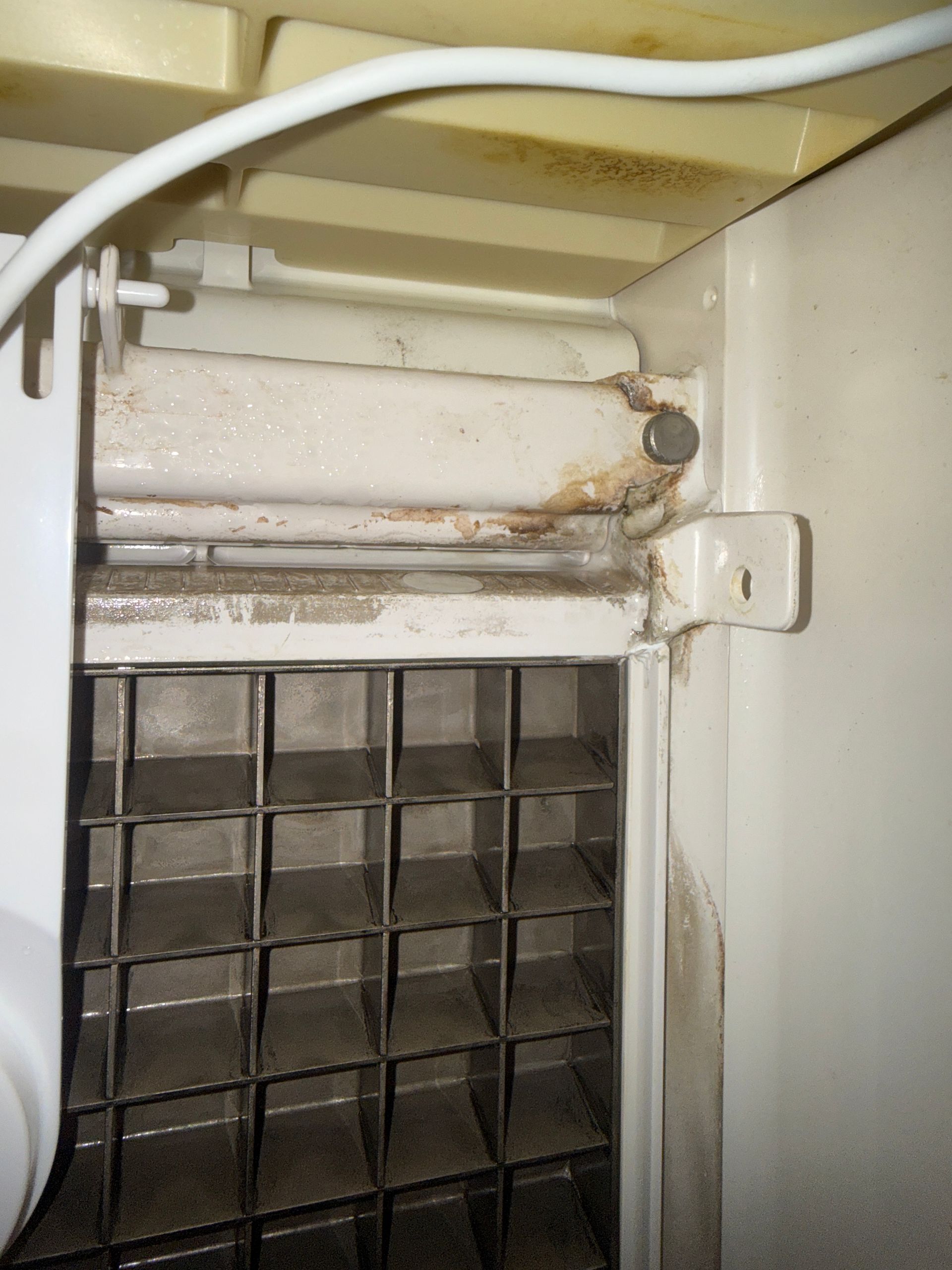 Close-up of a dusty vent or filter inside a white appliance or wall unit.