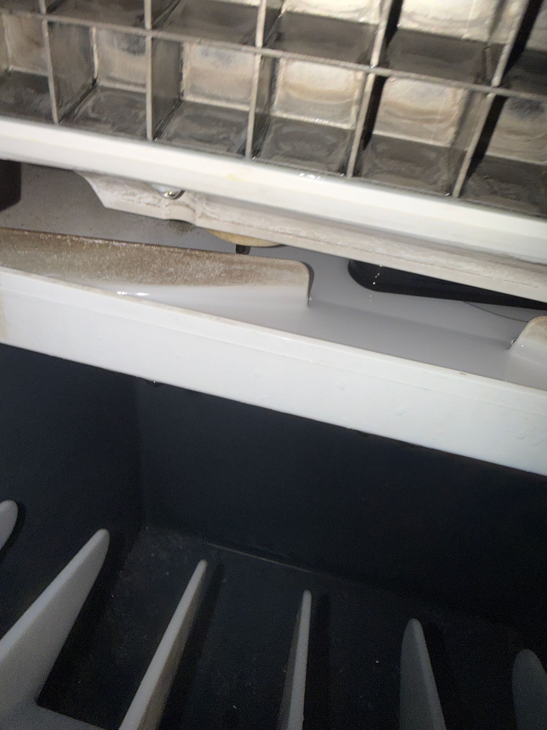 Close-up of a dusty air vent and black slats inside a white appliance or HVAC unit