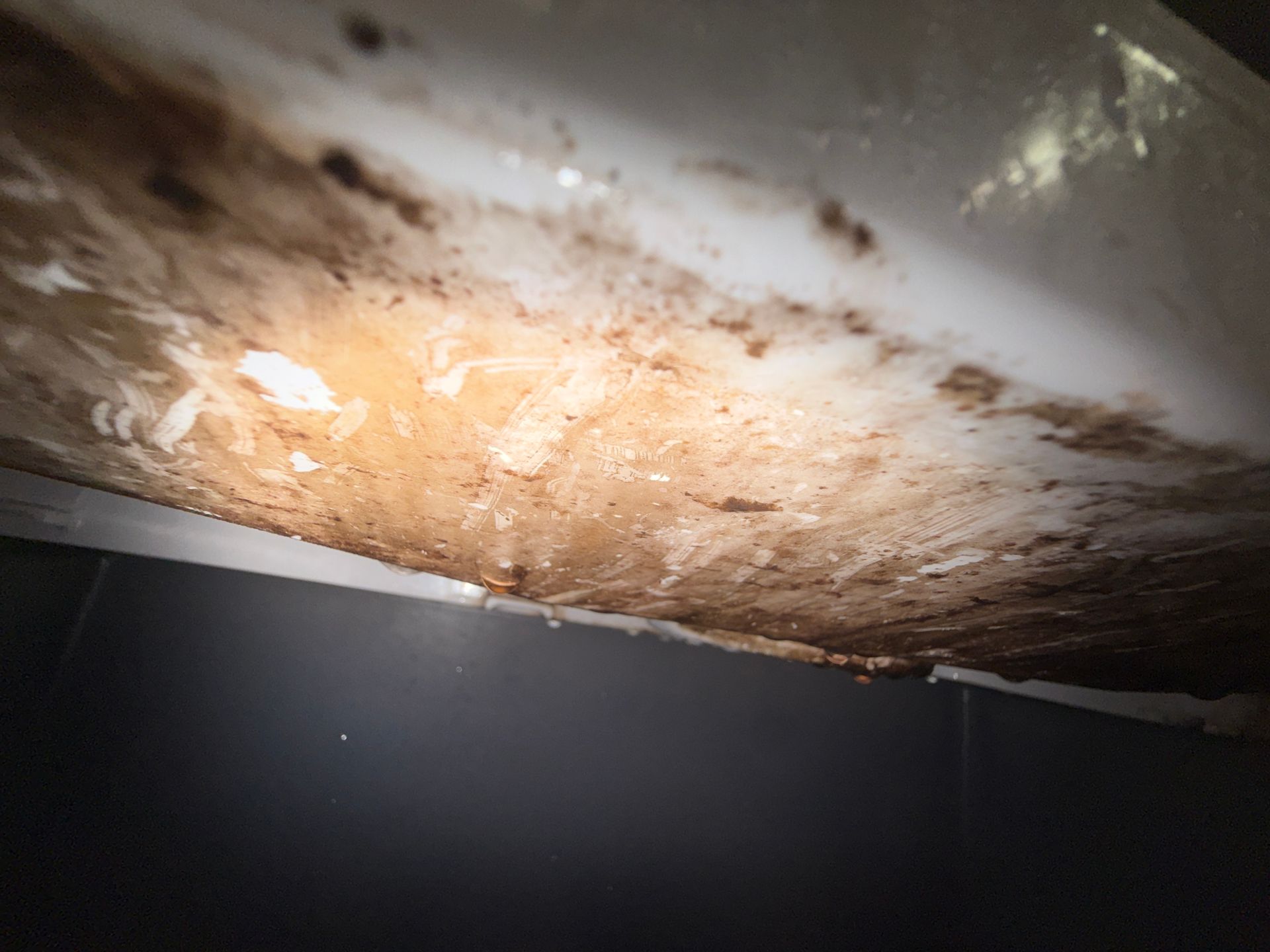 Close-up of a rusty, stained metal surface with bright light reflecting off it.