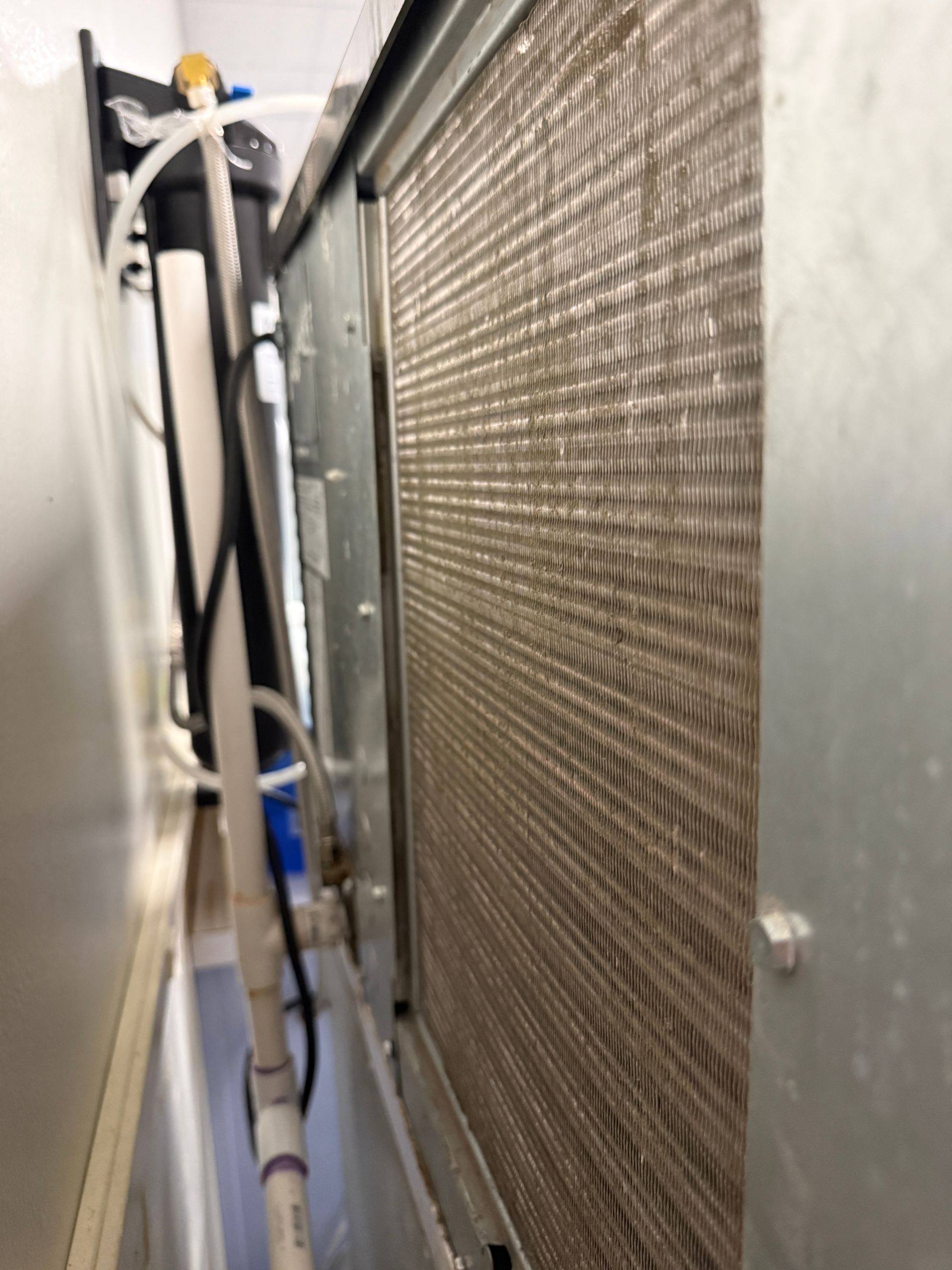 Close-up of a dusty HVAC or radiator coil beside cables in a narrow utility space