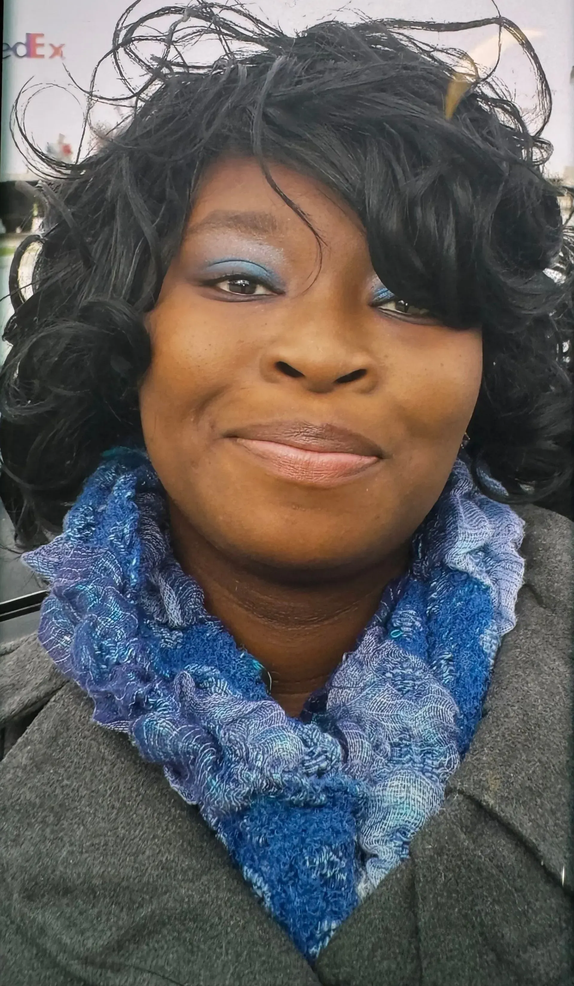 Smiling woman in a black coat and blue scarf against a light background
