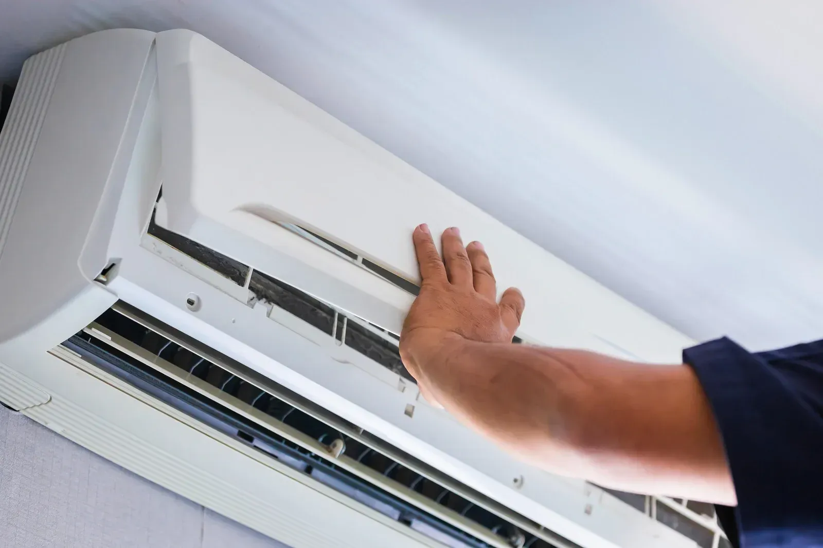 Hand adjusting the air conditioner vent on a wall-mounted unit