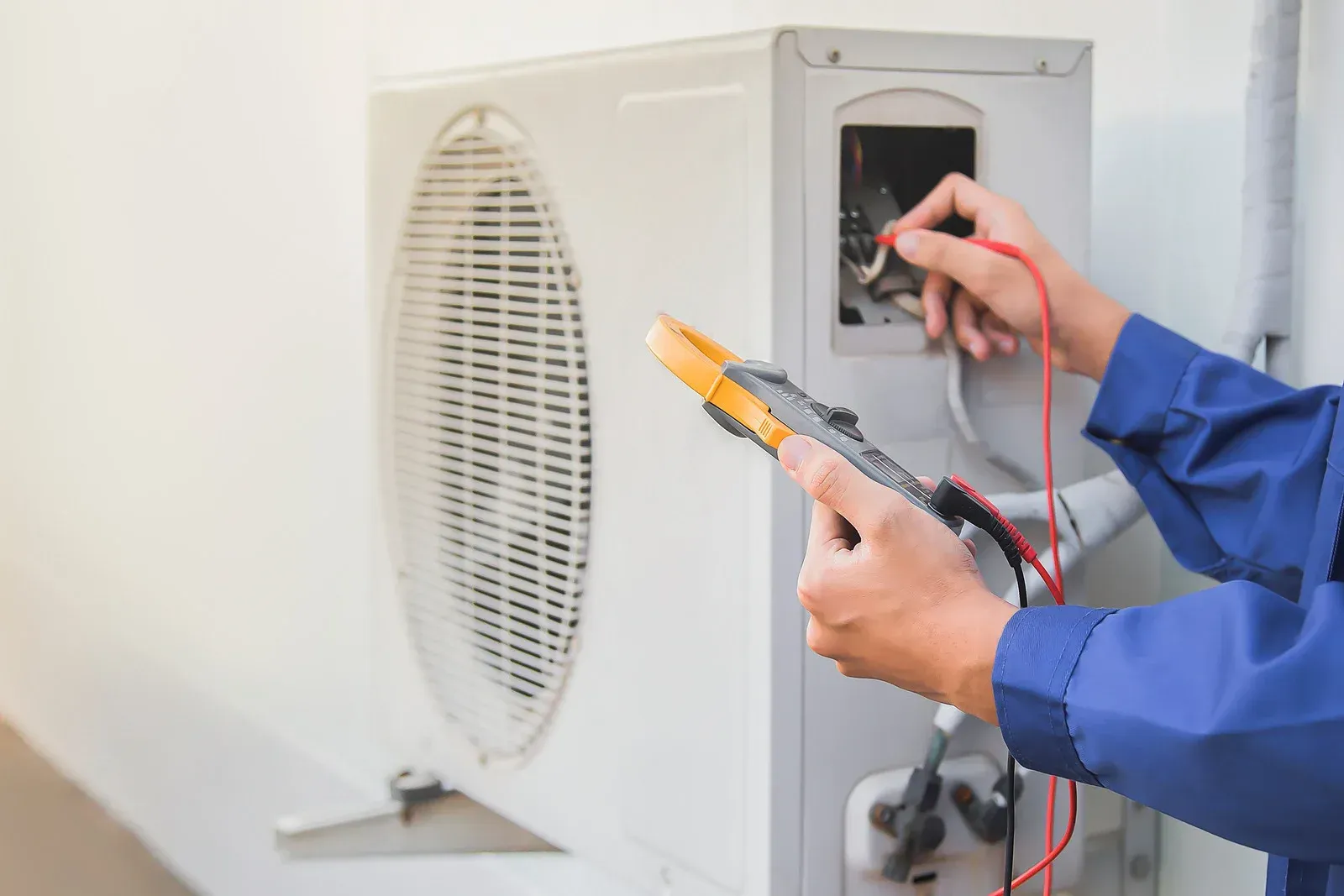 Technician testing an outdoor air conditioner unit with a multimeter and probes