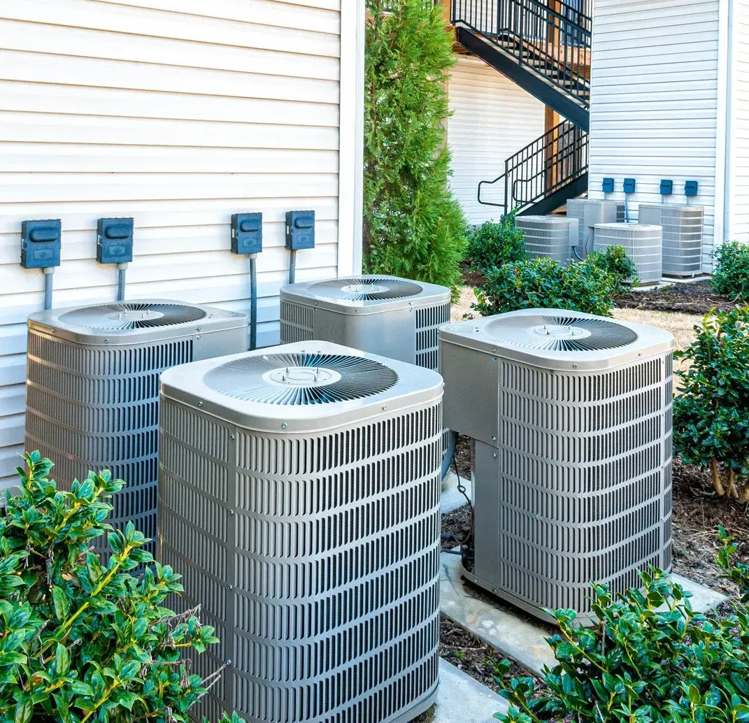 Outdoor HVAC condenser units beside a building with siding and an exterior staircase