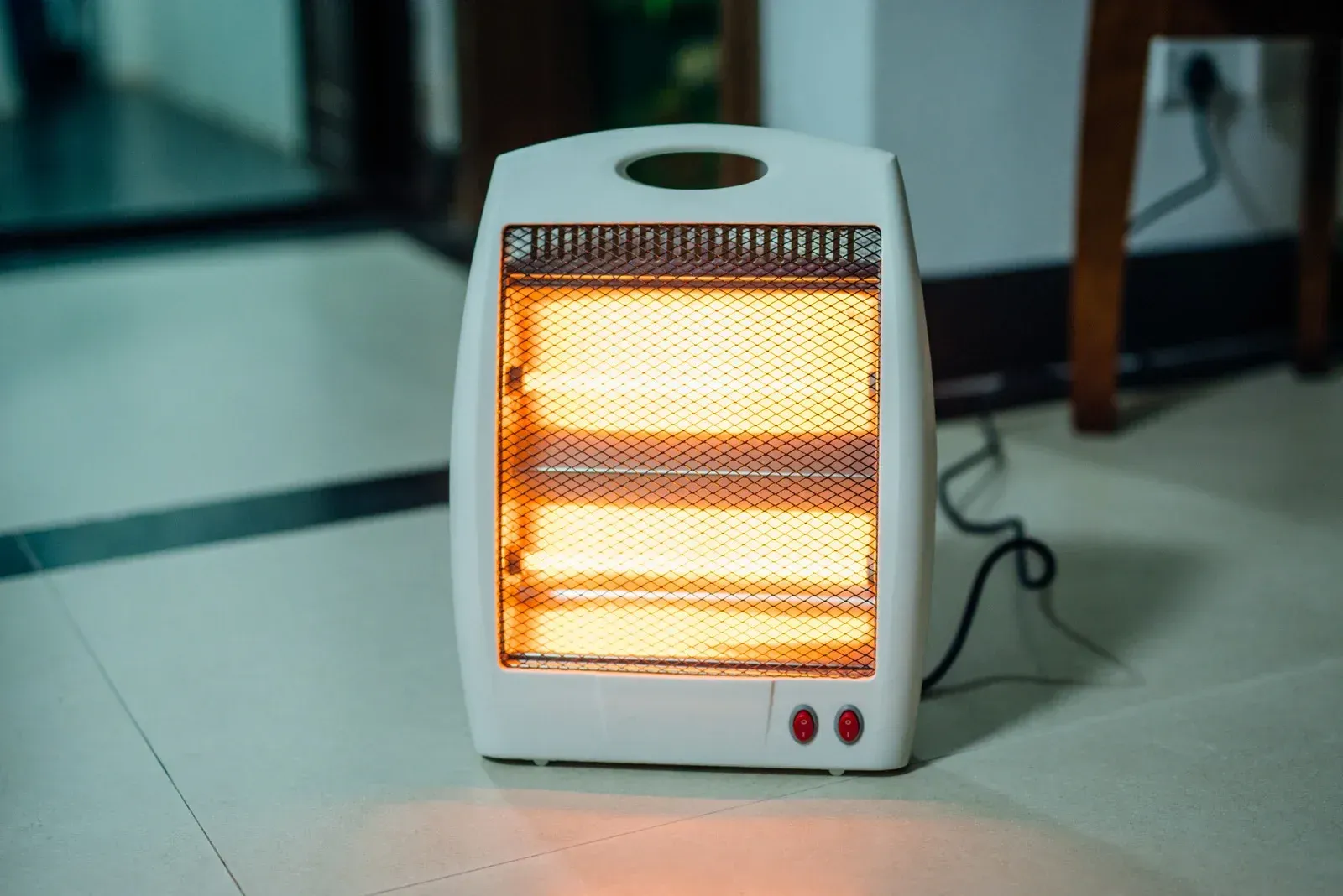 Small white space heater glowing orange on a tiled floor indoors
