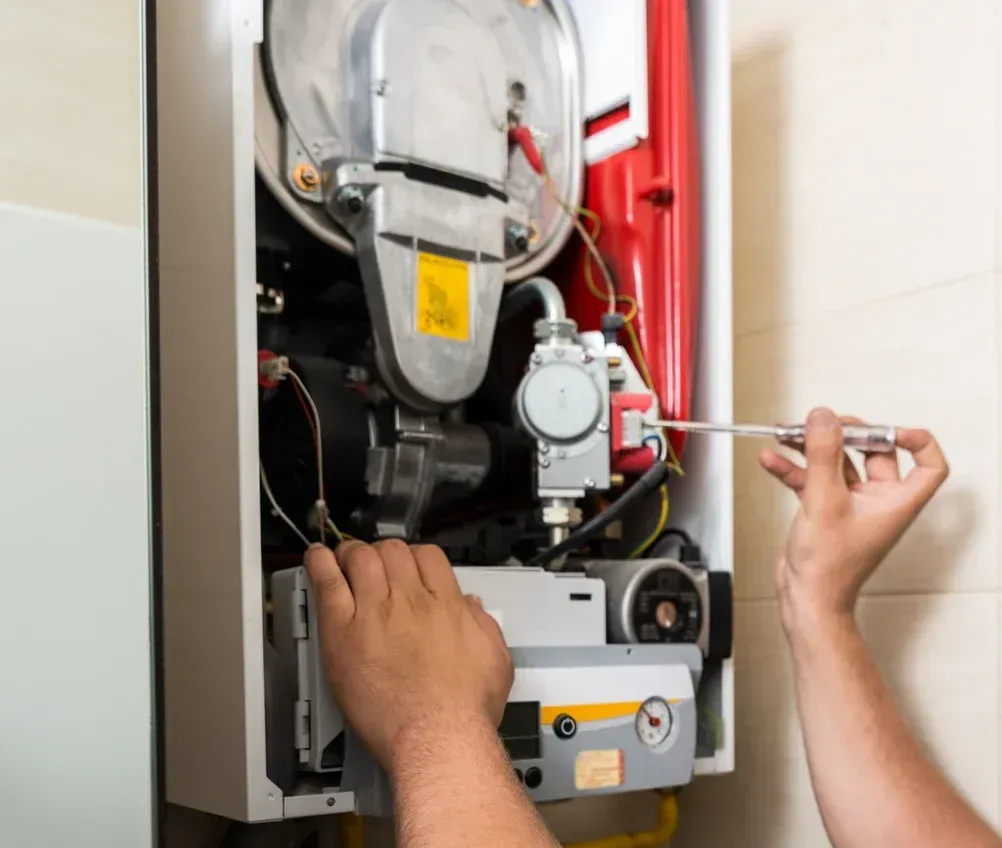 Technician repairing open wall-mounted boiler with tools inside a utility cabinet