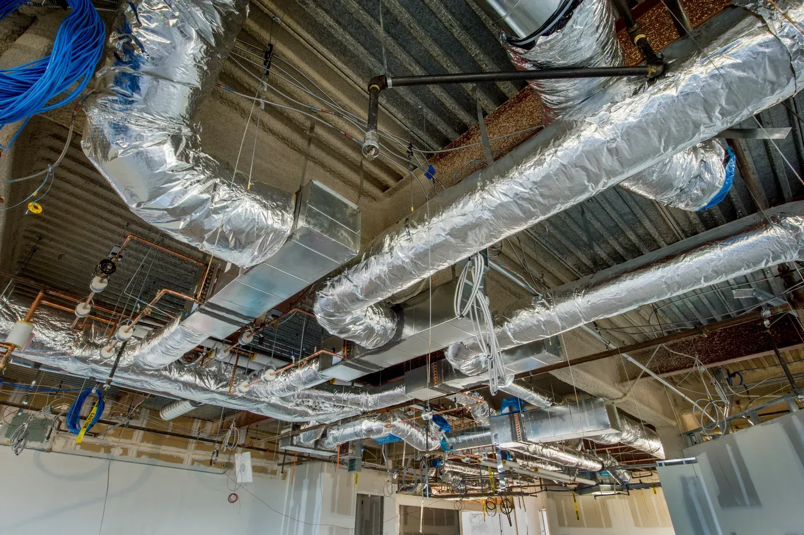 Industrial ceiling with exposed silver HVAC ducts, pipes, and wiring in a building under construction