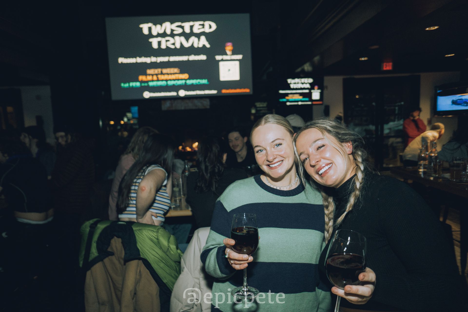 Two women are posing for a picture in front of a sign that says twisted trivia.