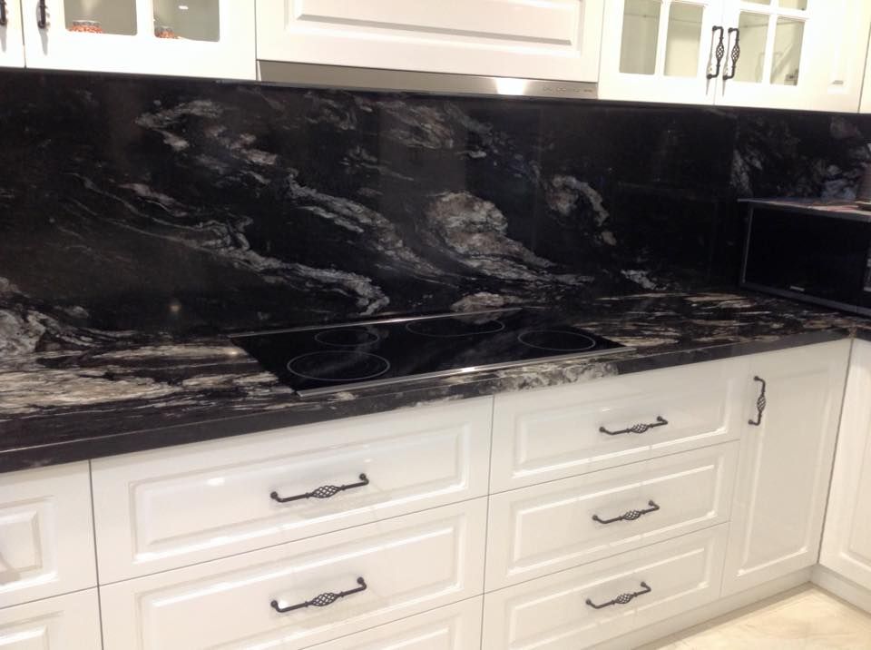 A kitchen with black granite counter tops and white cabinets.