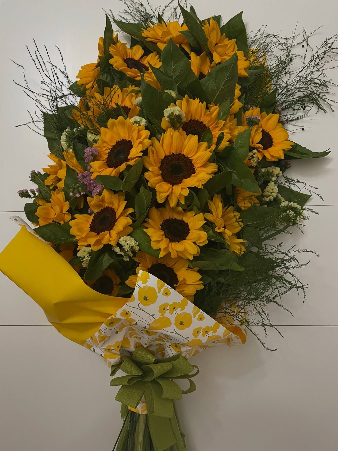 Mazzo di girasoli avvolto in carta gialla e bianca, legato con un nastro verde.