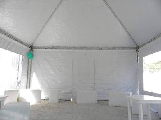 Interior vacío de una tienda de campaña blanca con mesas plegables, bancos y una linterna verde colgando de la estructura.