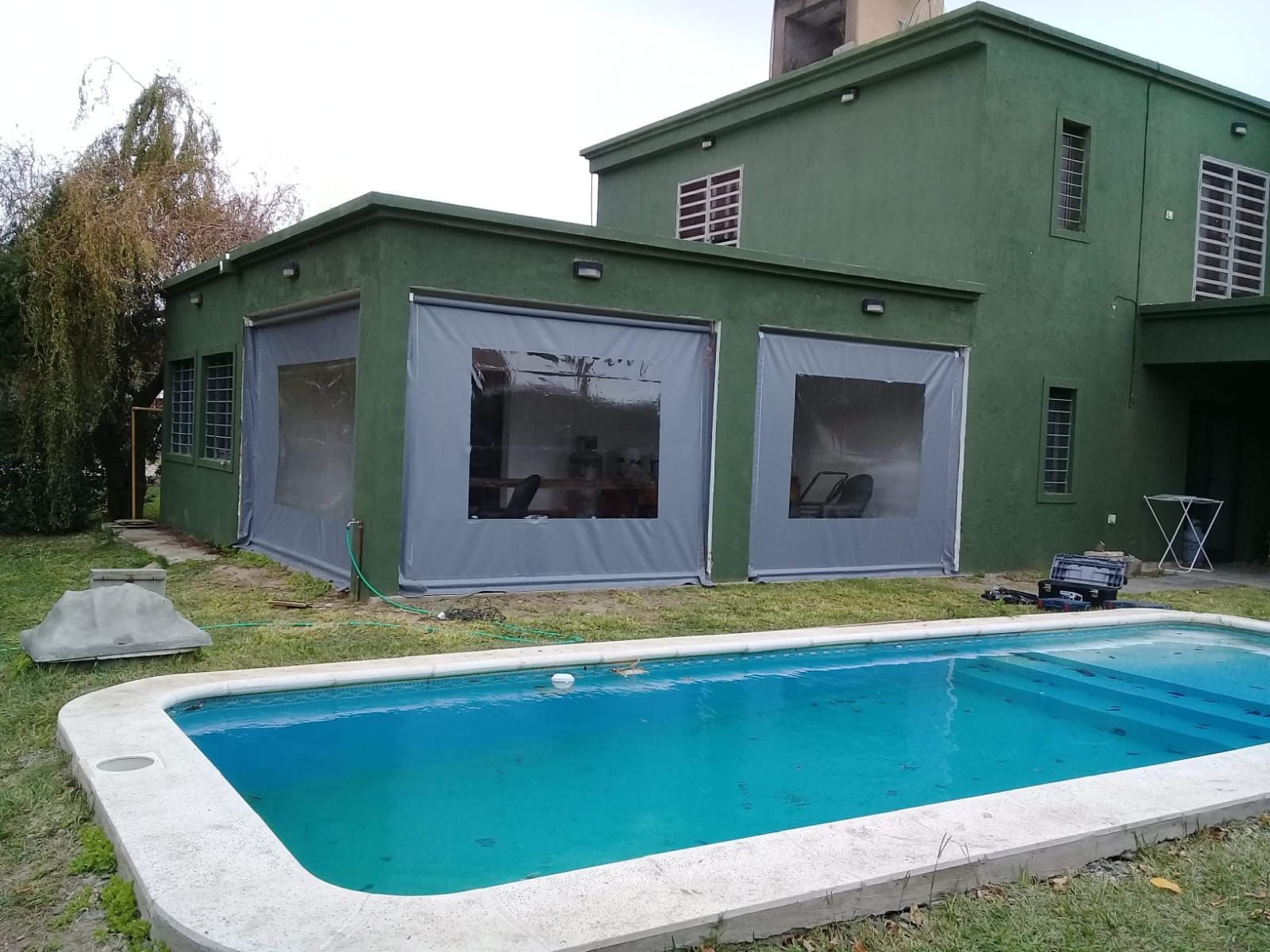 Casa con patio trasero, piscina azul y paredes exteriores verdes.