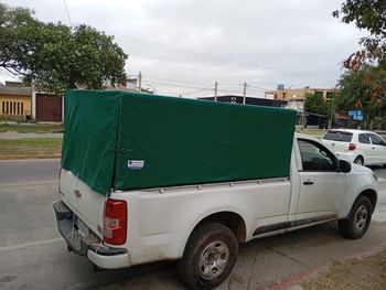 Camioneta blanca con caja de carga cubierta de color verde estacionada en una calle