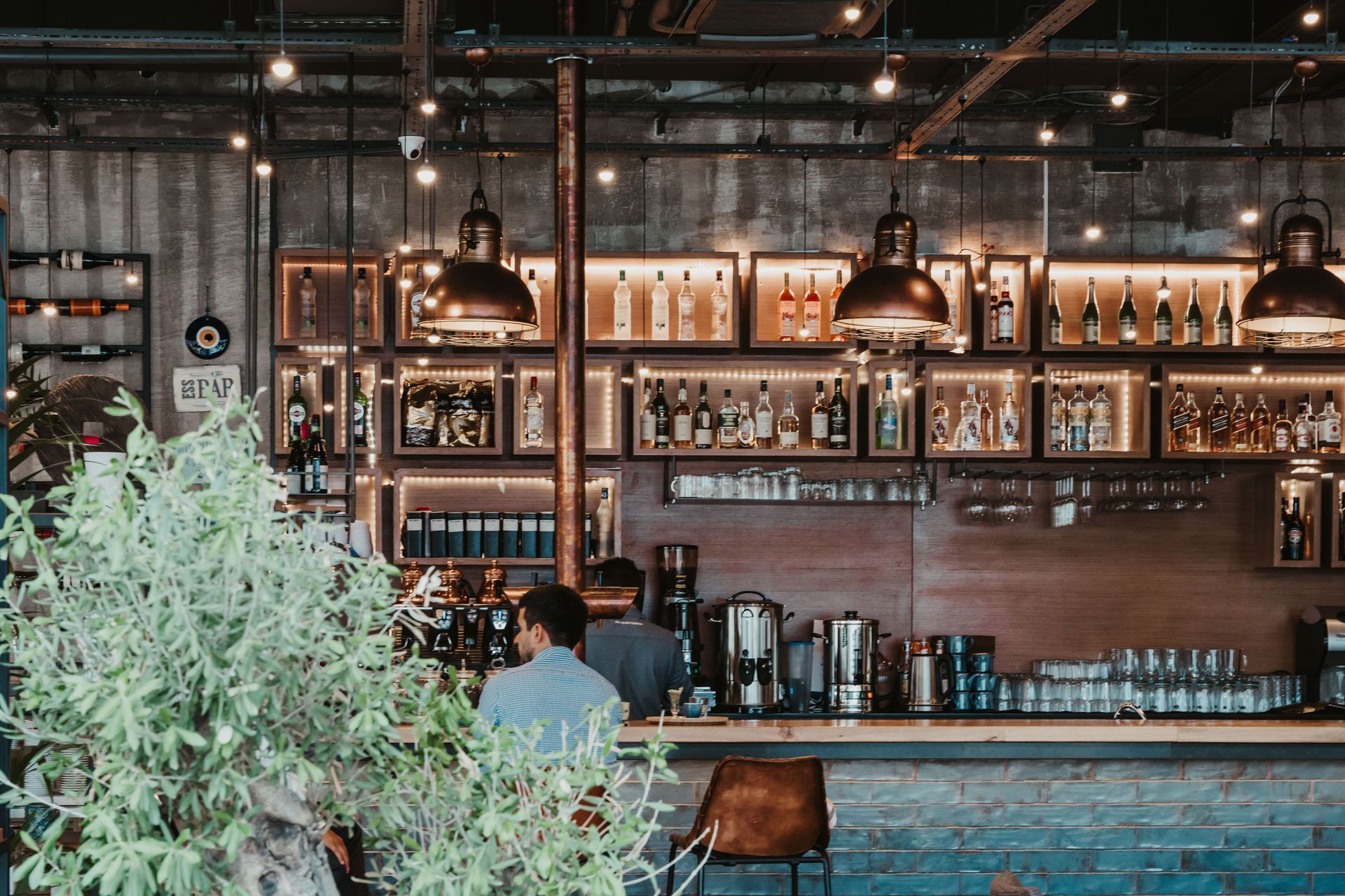 Cozy café bar with shelves of bottles, warm pendant lights, and a seated person at the counter
