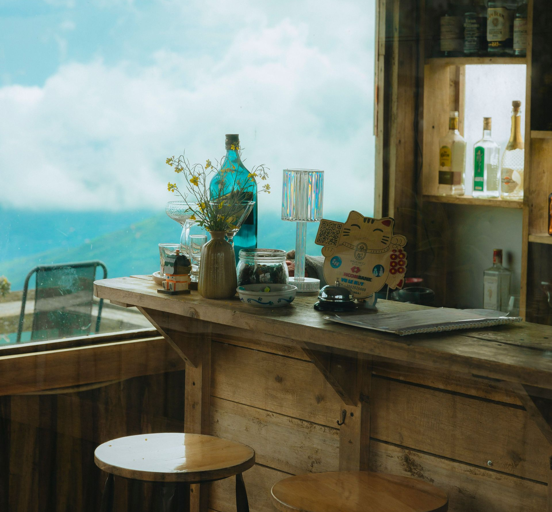 Rustic seaside café bar by a window, with bottles and decor overlooking the water.
