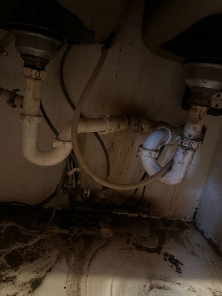 Under-sink plumbing with two drains, exposed pipes, and visible water damage or mold on the cabinet floor.