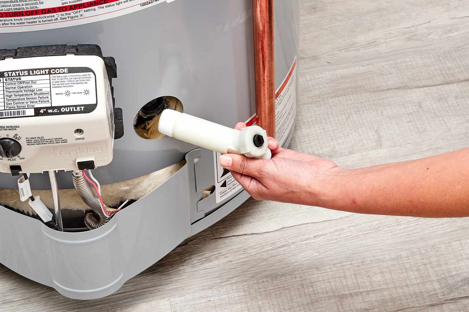 Person holding a white pipe near a wall-mounted appliance with exposed wiring under a gray cover