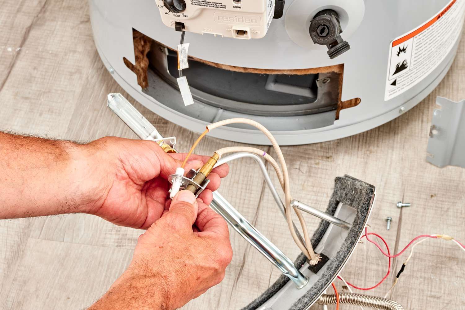 Hands connecting wires to a water heater’s open panel during repair