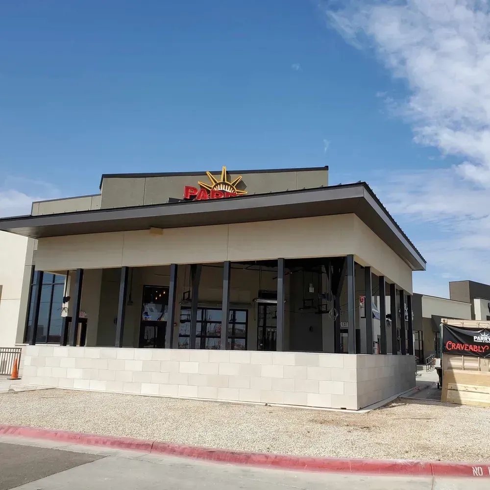 Modern fast-food restaurant exterior with a white facade, glass windows, and red sign under a blue sky