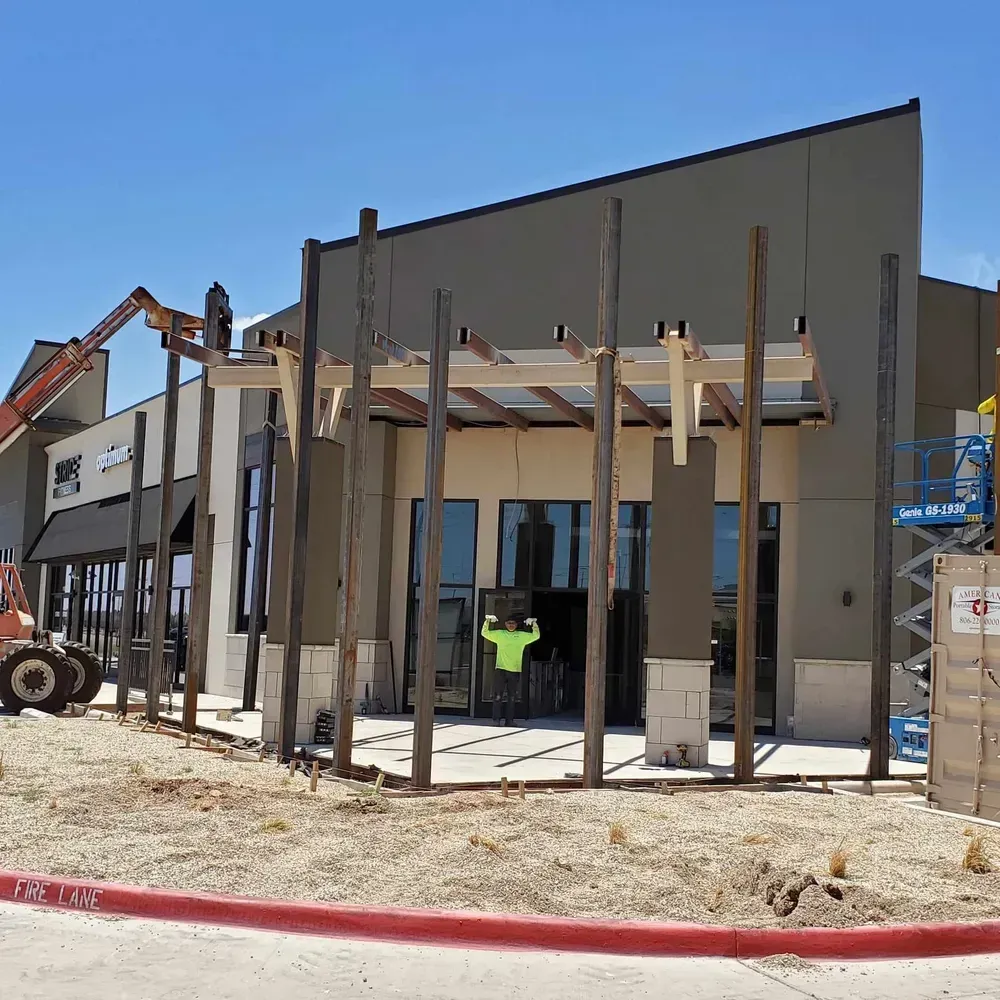 Construction site with steel framing in front of a building and a worker in a neon safety shirt.