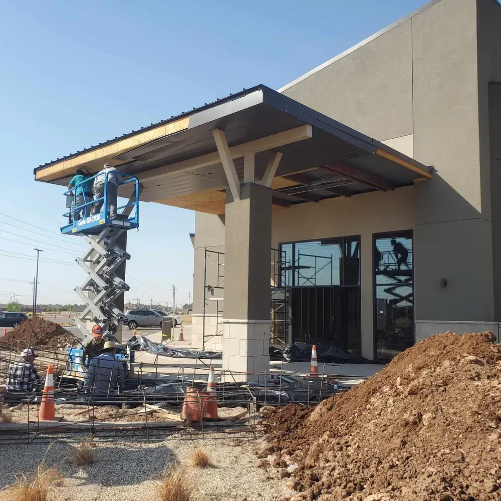 Construction site with a scissor lift under a new building canopy and piles of dirt in front