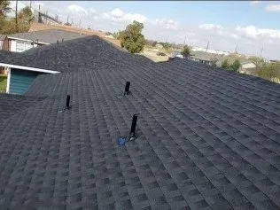 Black shingle roof with several vent pipes under a partly cloudy sky