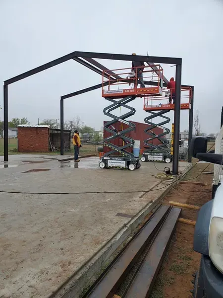 Construction lift inside a steel frame on a wet concrete site, with workers and materials nearby