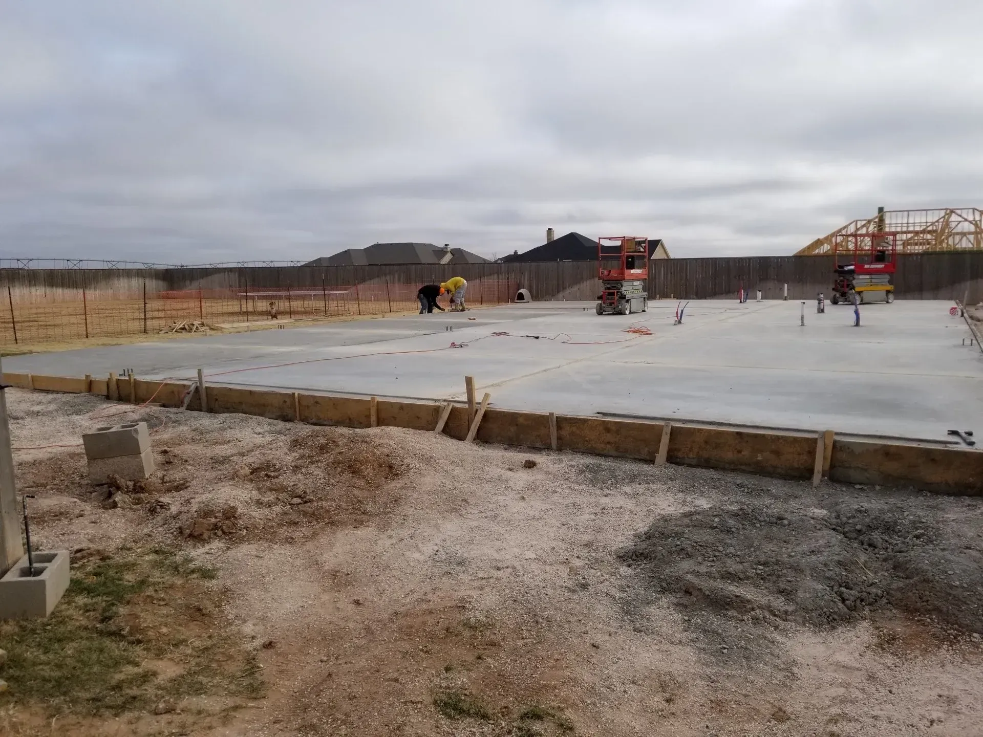 Construction site with fresh concrete slab, workers, and machinery under a cloudy sky