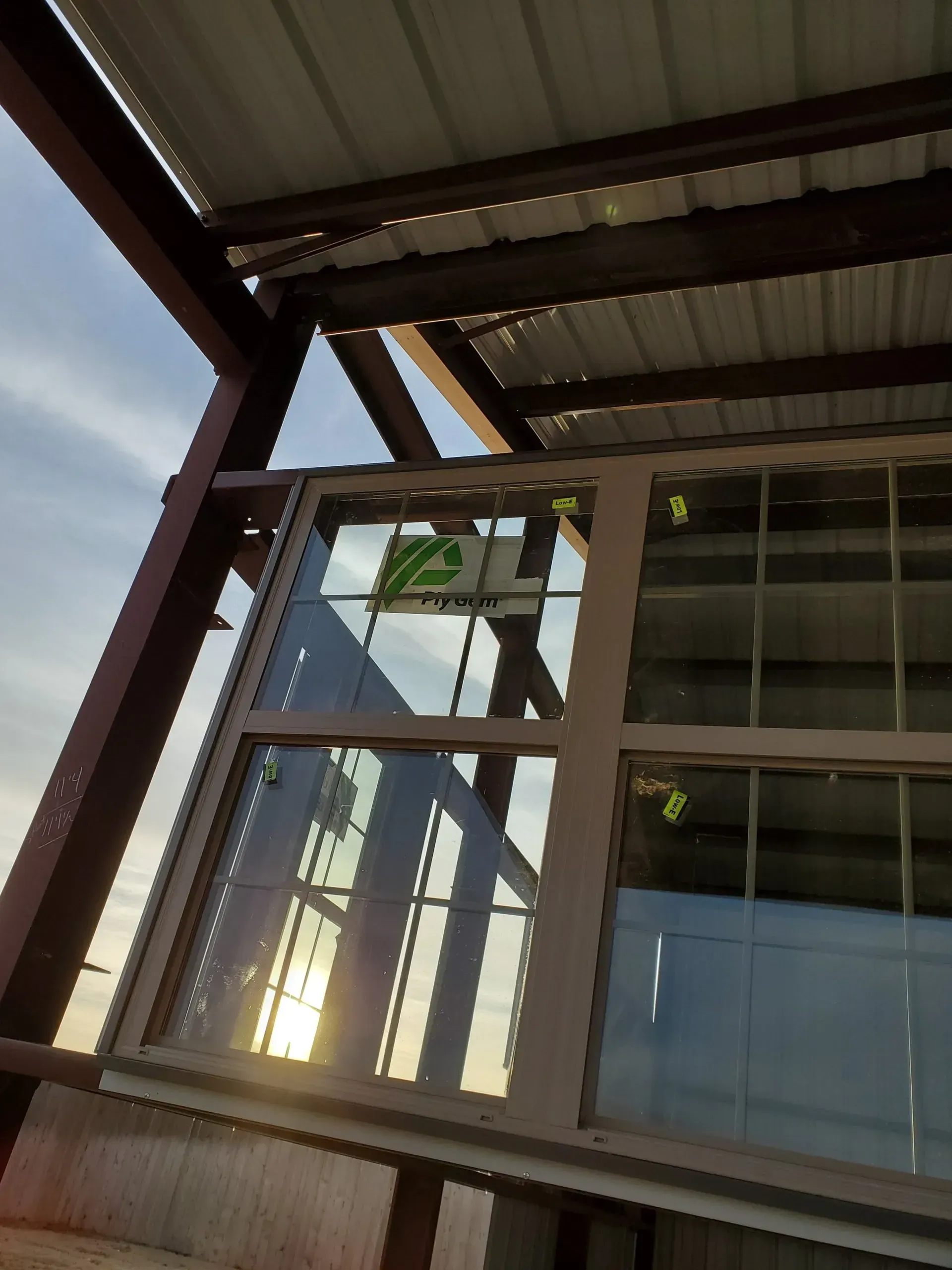 Looking up at a glass-and-metal building corner with window reflections and a corrugated roof overhead