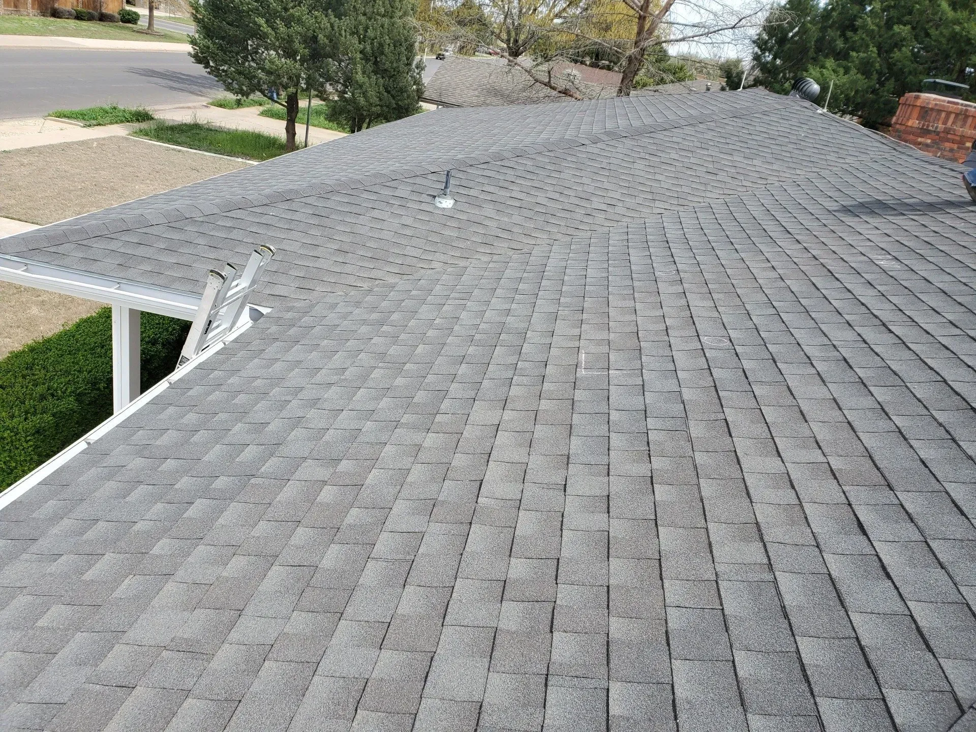 Gray shingled roof viewed from above with trees and a small section of gutter visible