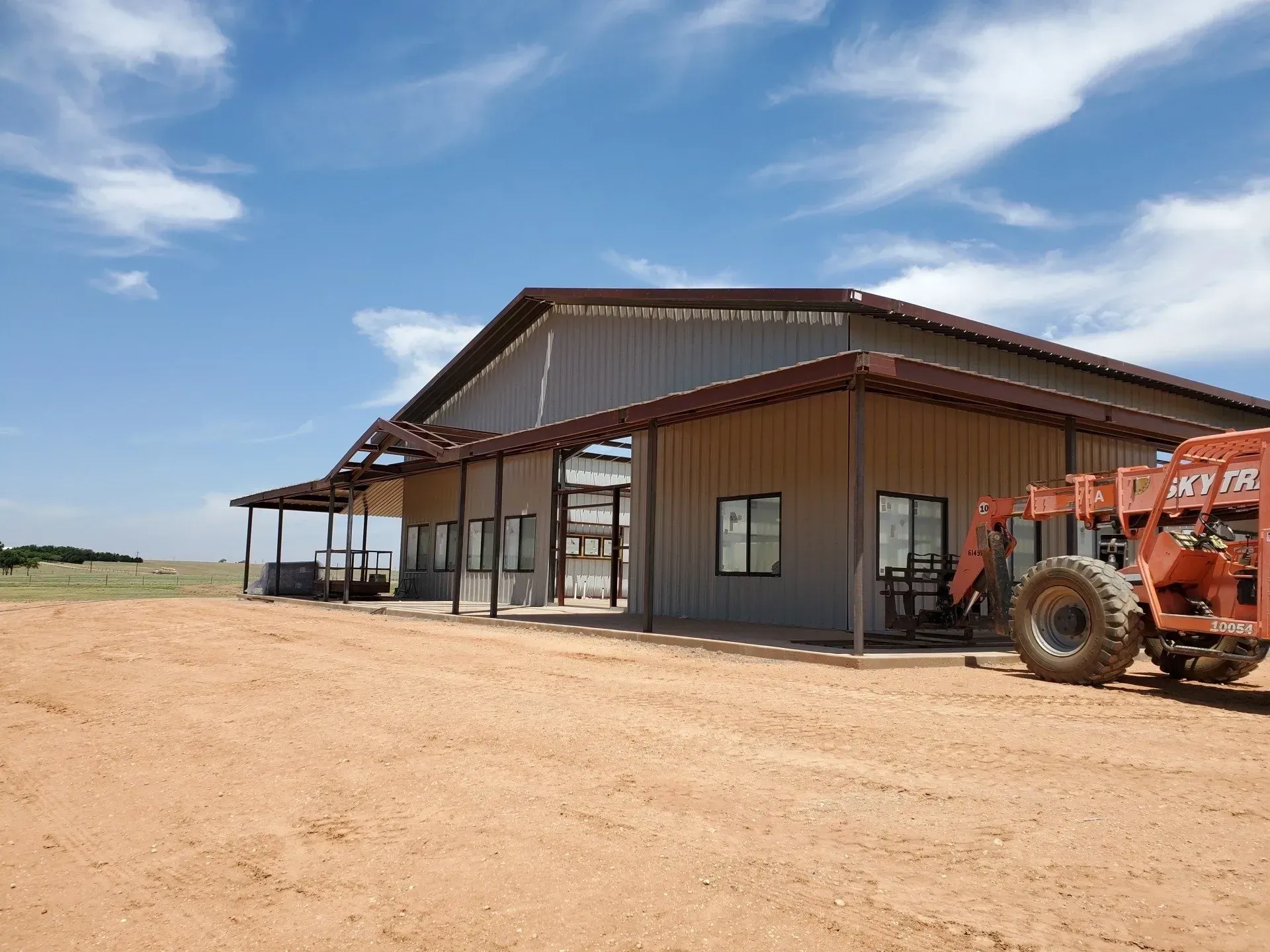 Rustic farm building with a red tractor parked outside on a dusty lot under a blue sky