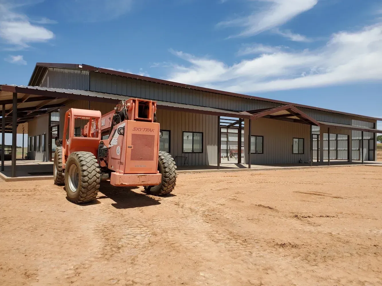Orange construction vehicle in front of a tan building under a blue sky