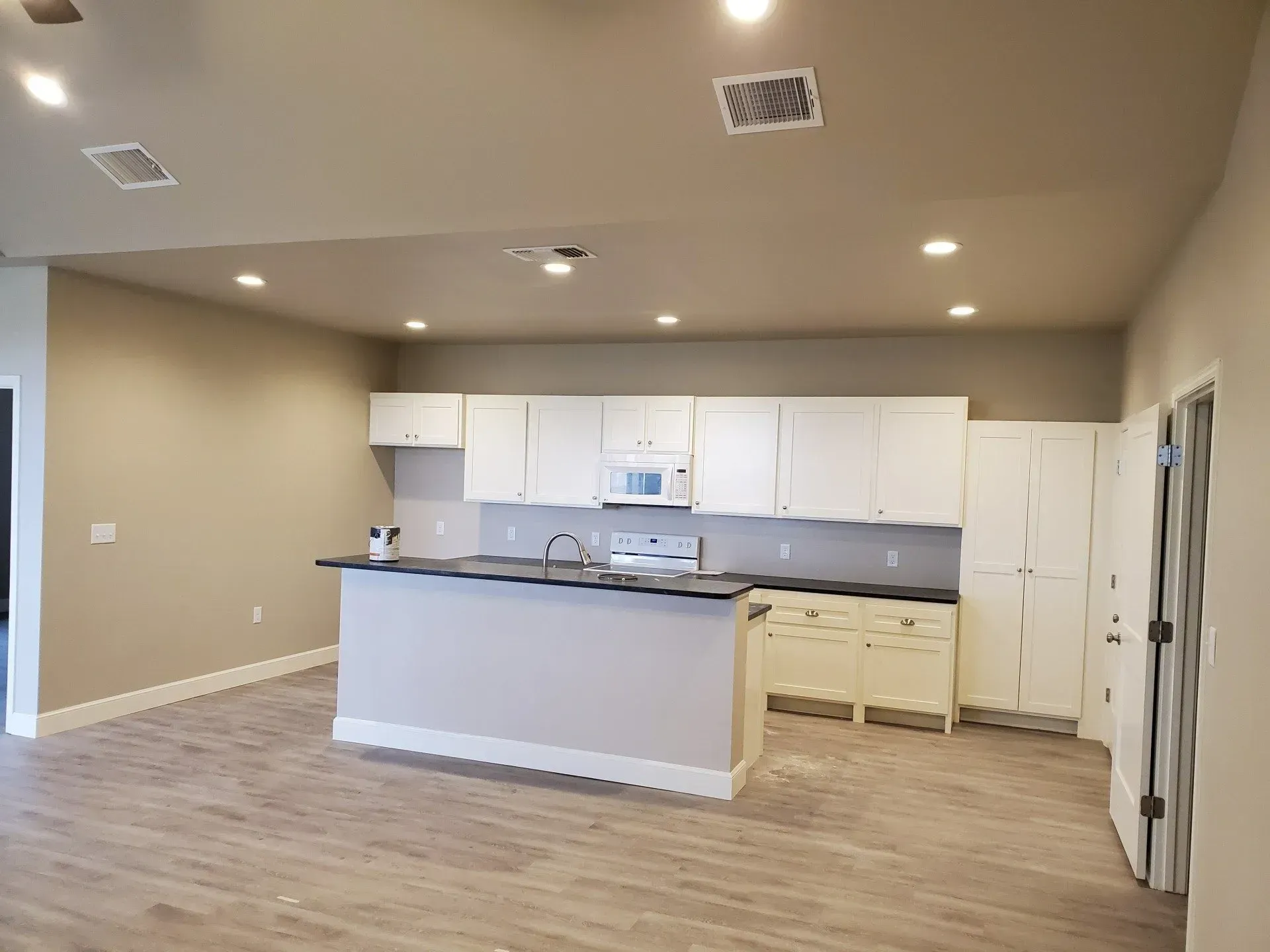 Empty modern kitchen with white cabinets, gray countertops, and wood flooring in an open living space