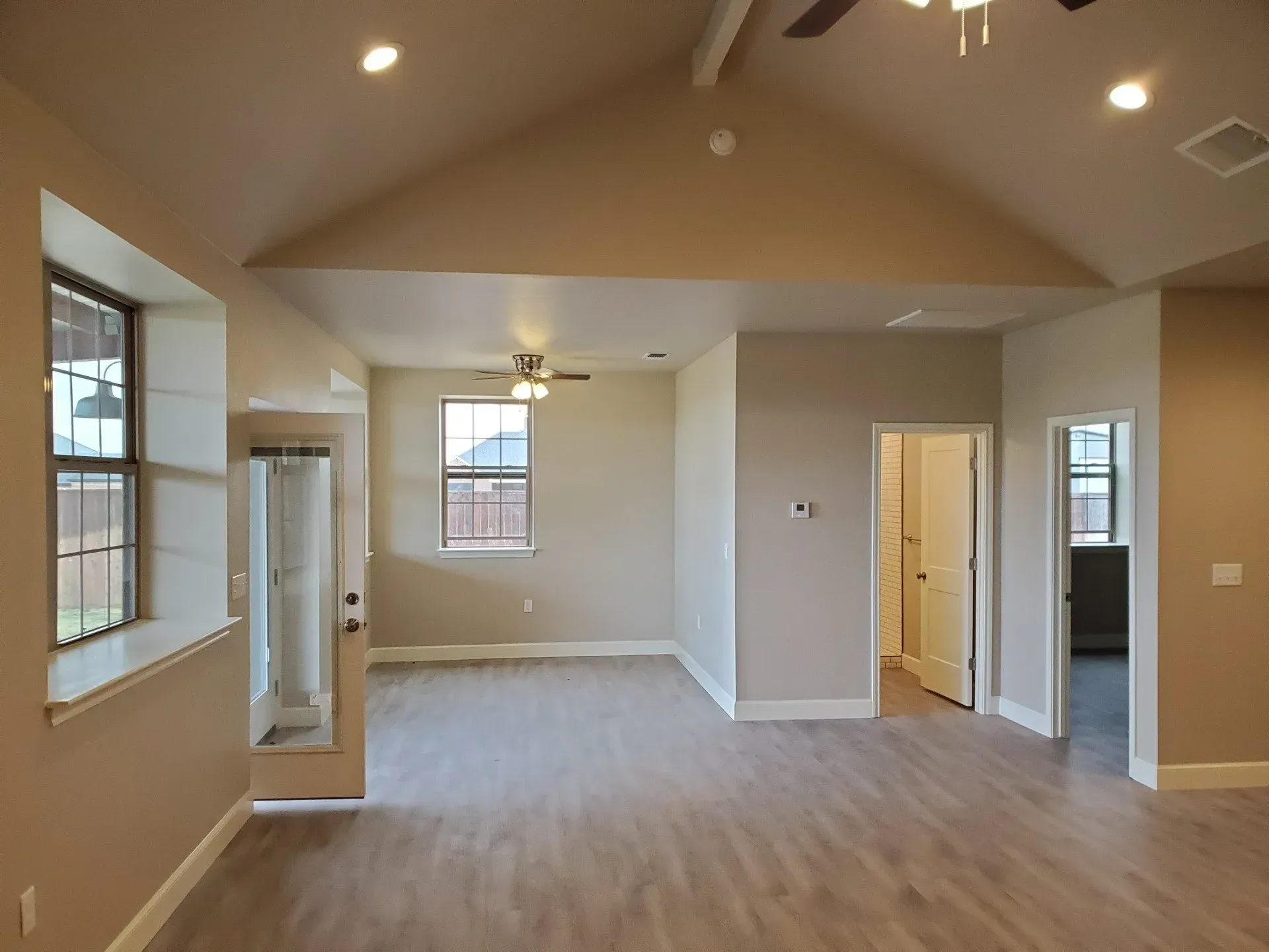 Empty beige living room with vaulted ceiling, ceiling fan, recessed lights, and carpeted floor.