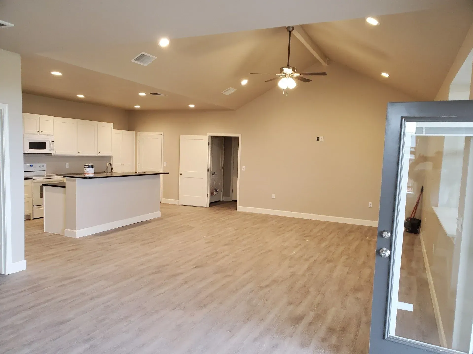 Empty open-plan living room and kitchen with beige walls, light wood floors, and ceiling fan.