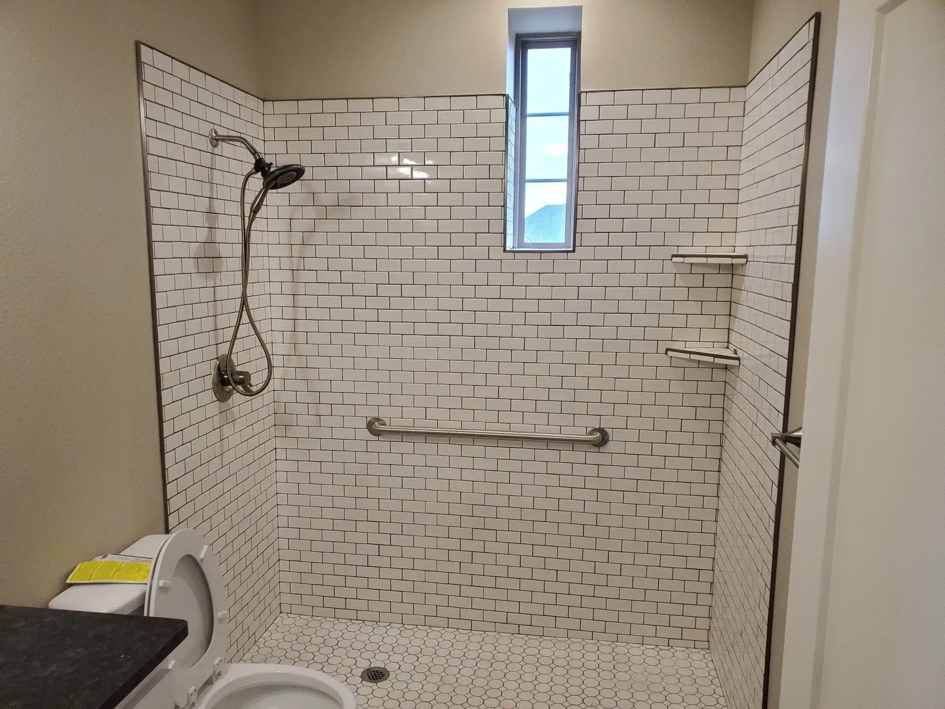 Bathroom shower with white subway tile, grab bars, handheld showerhead, and bench.