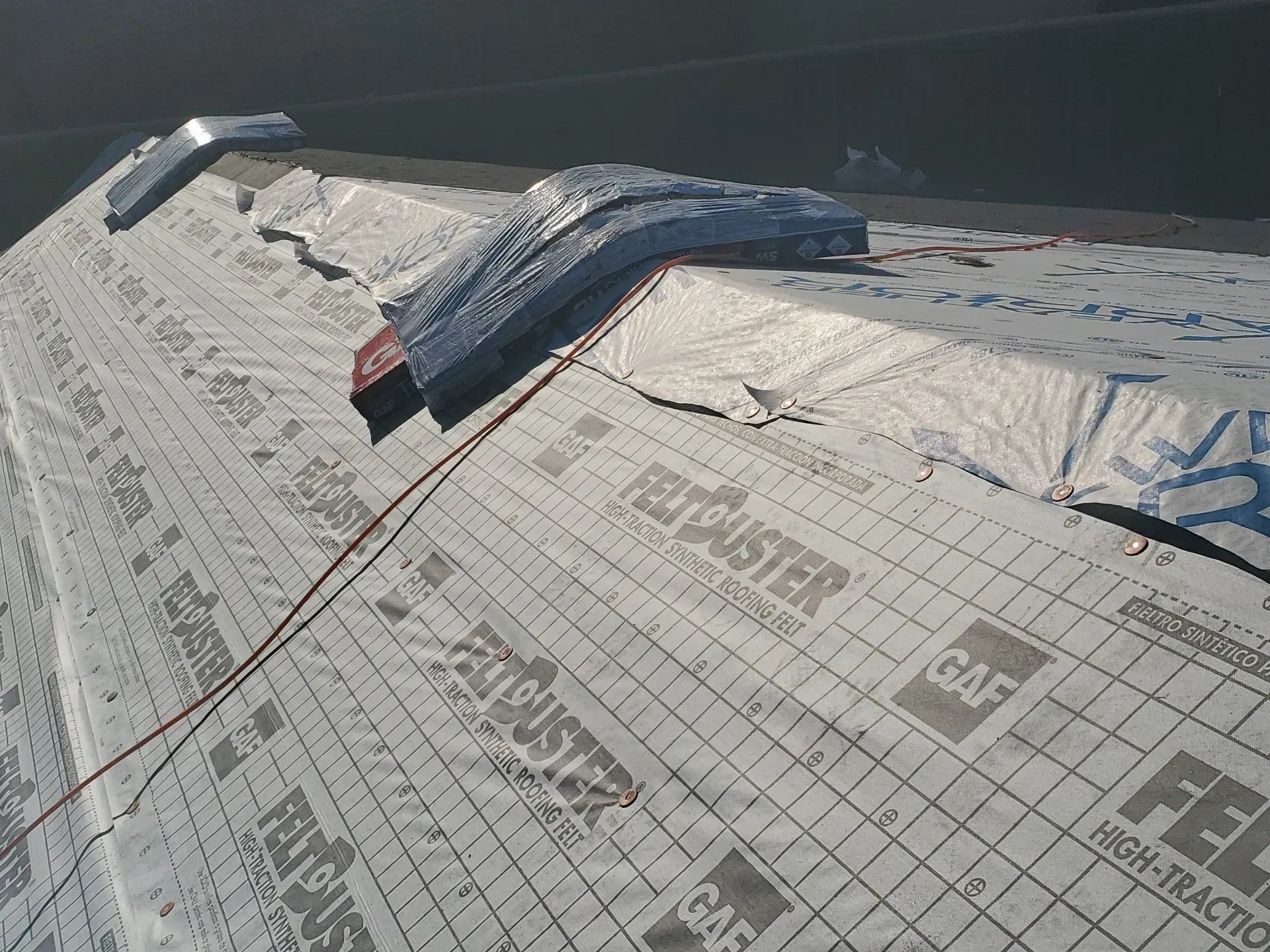 Roof under construction with white roofing underlayment and a blue tarp near the ridge.