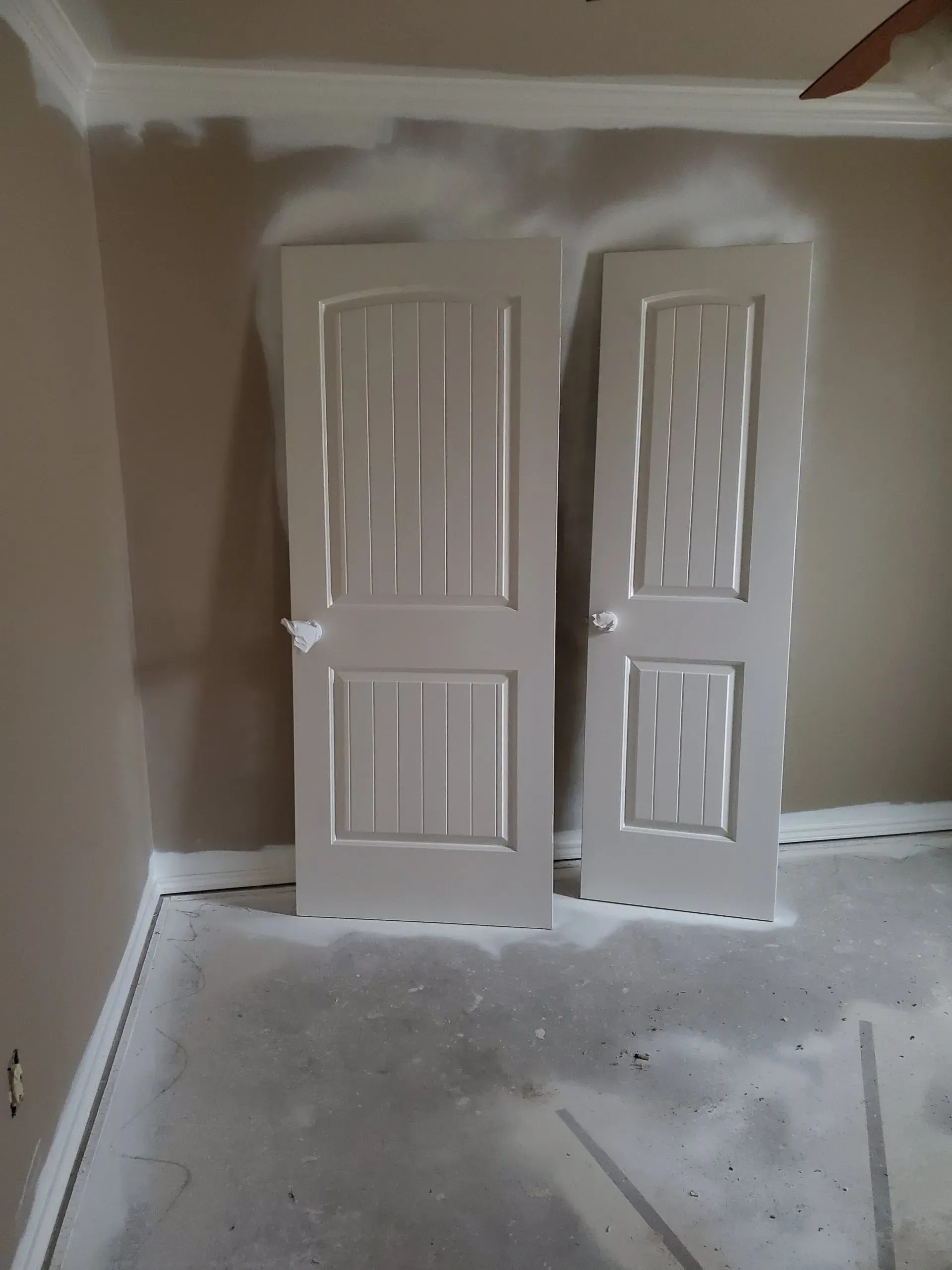 Two white closet doors leaning in an unfinished room with bare drywall and a concrete floor