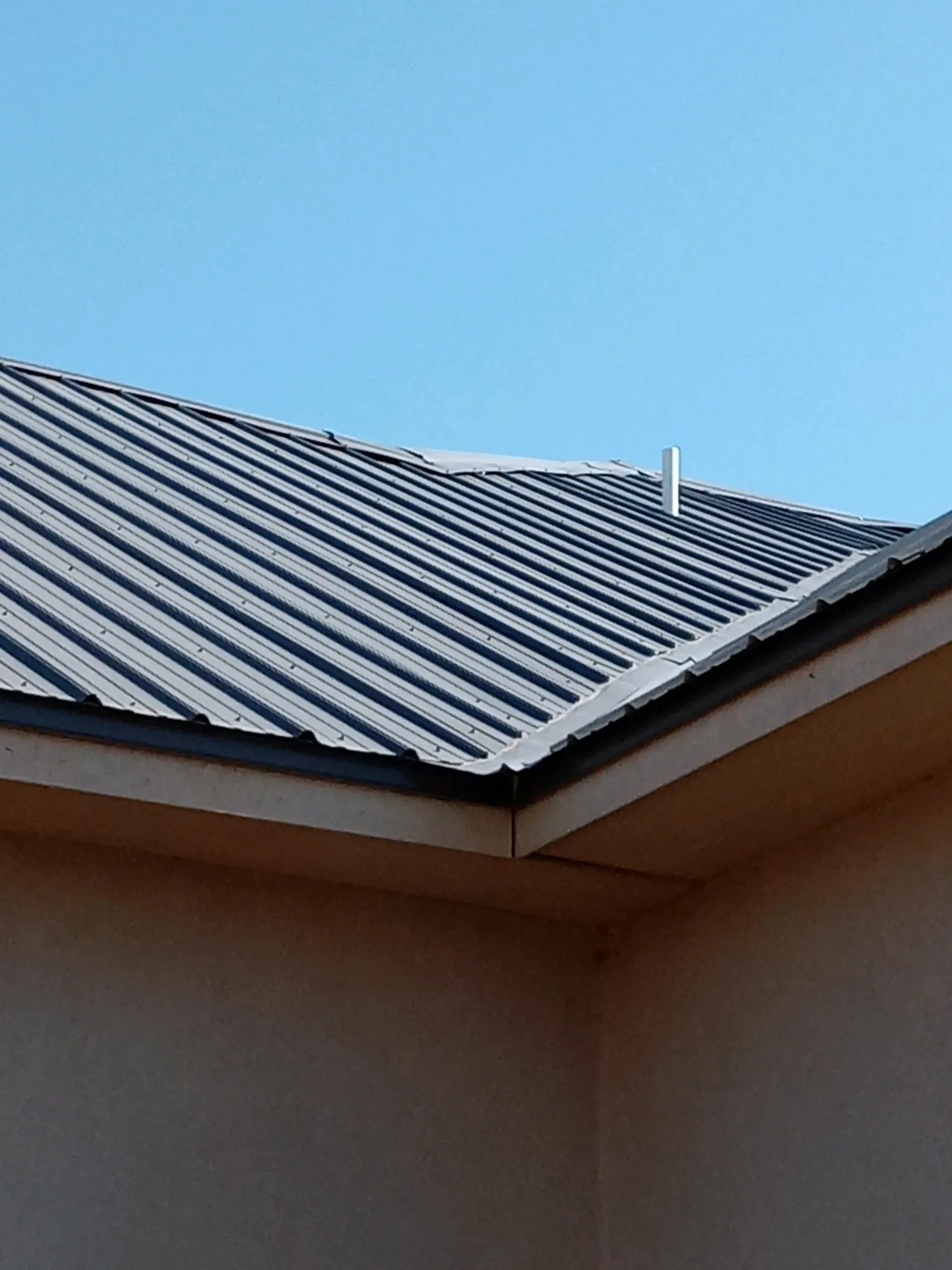 Blue corrugated metal roof against a clear sky above a beige building corner